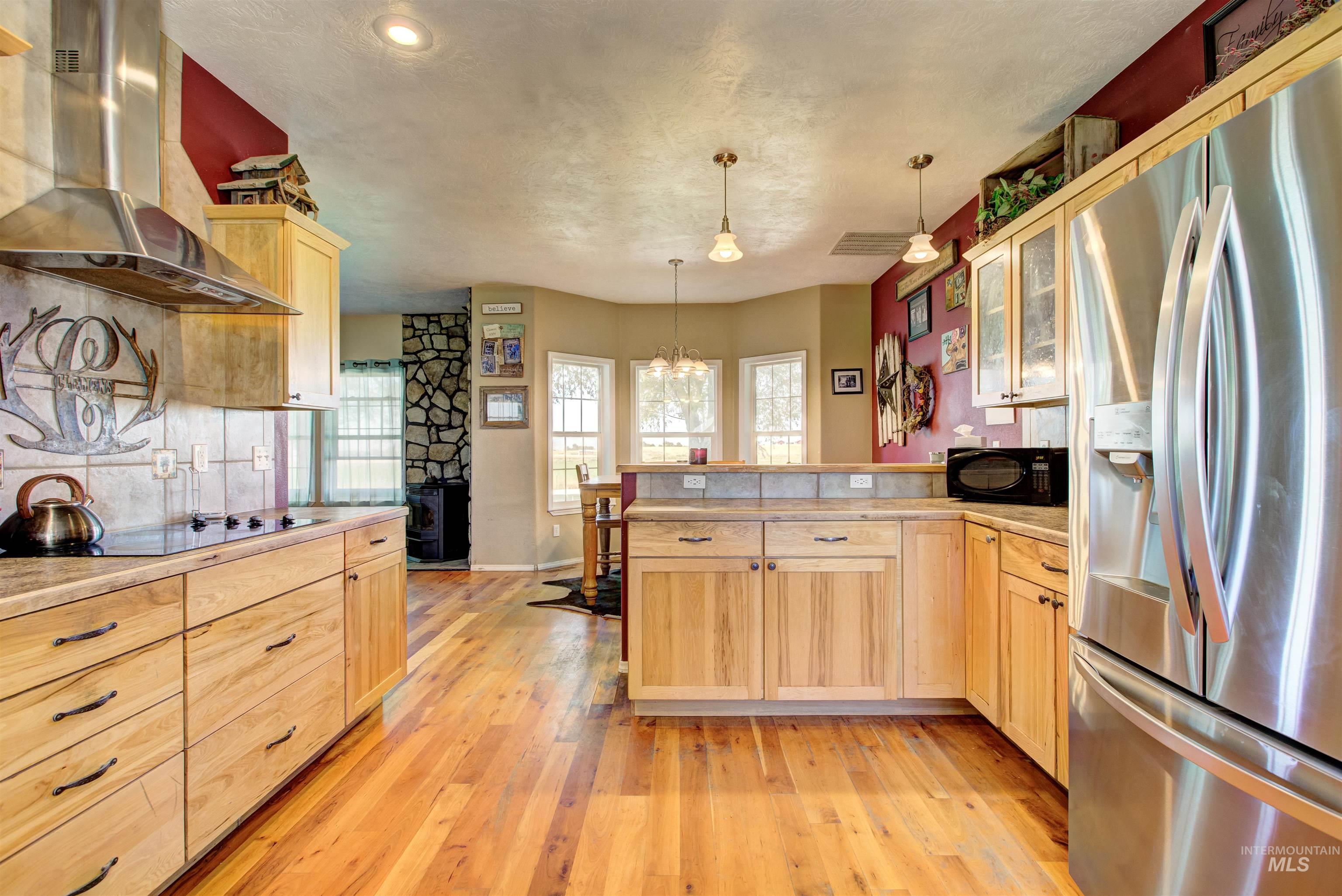 Kitchen featuring light brown cabinetry, black appliances, extractor fan, plenty of natural light, and a textured ceiling