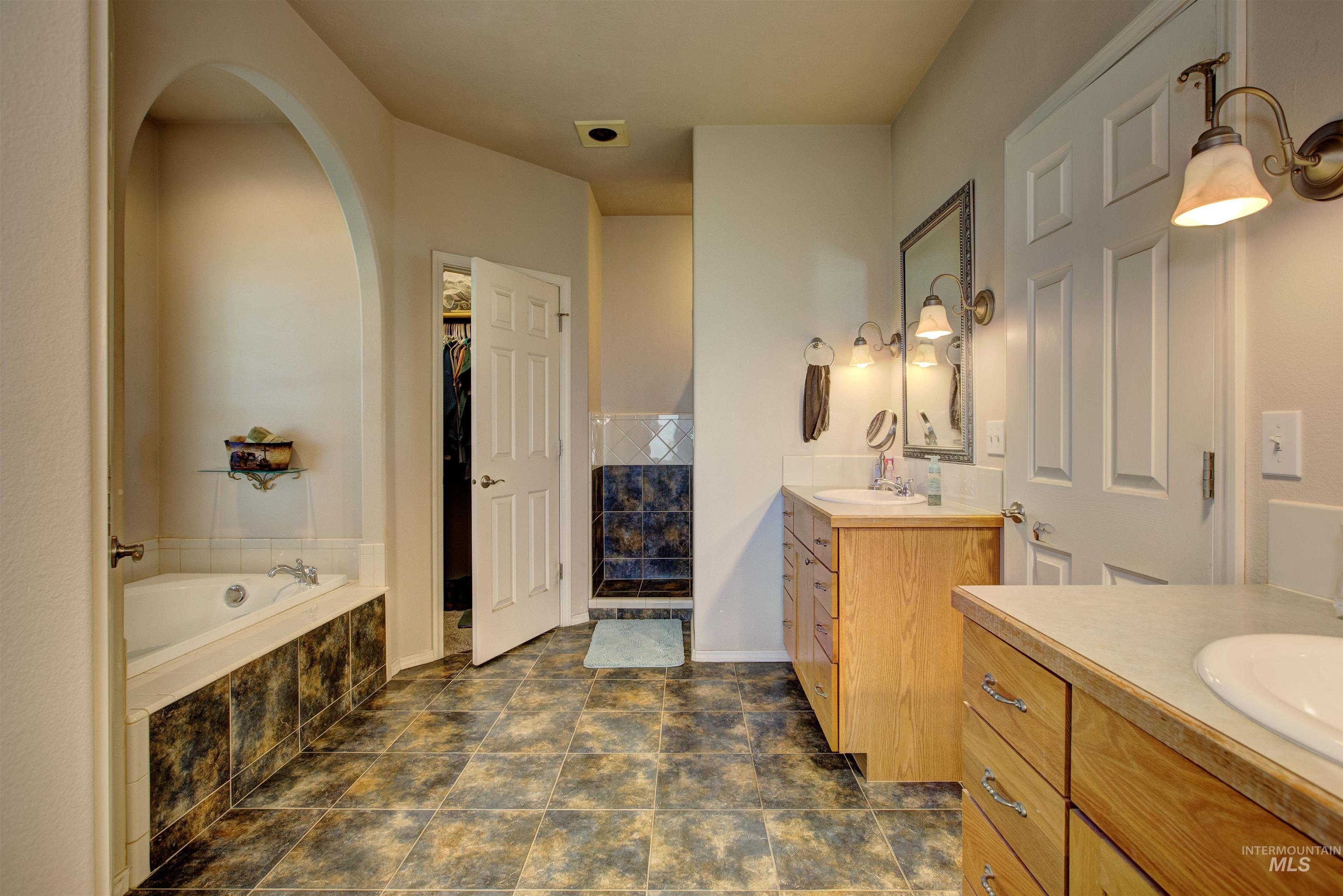 Full bath with two vanities, a garden tub, and a walk in closet