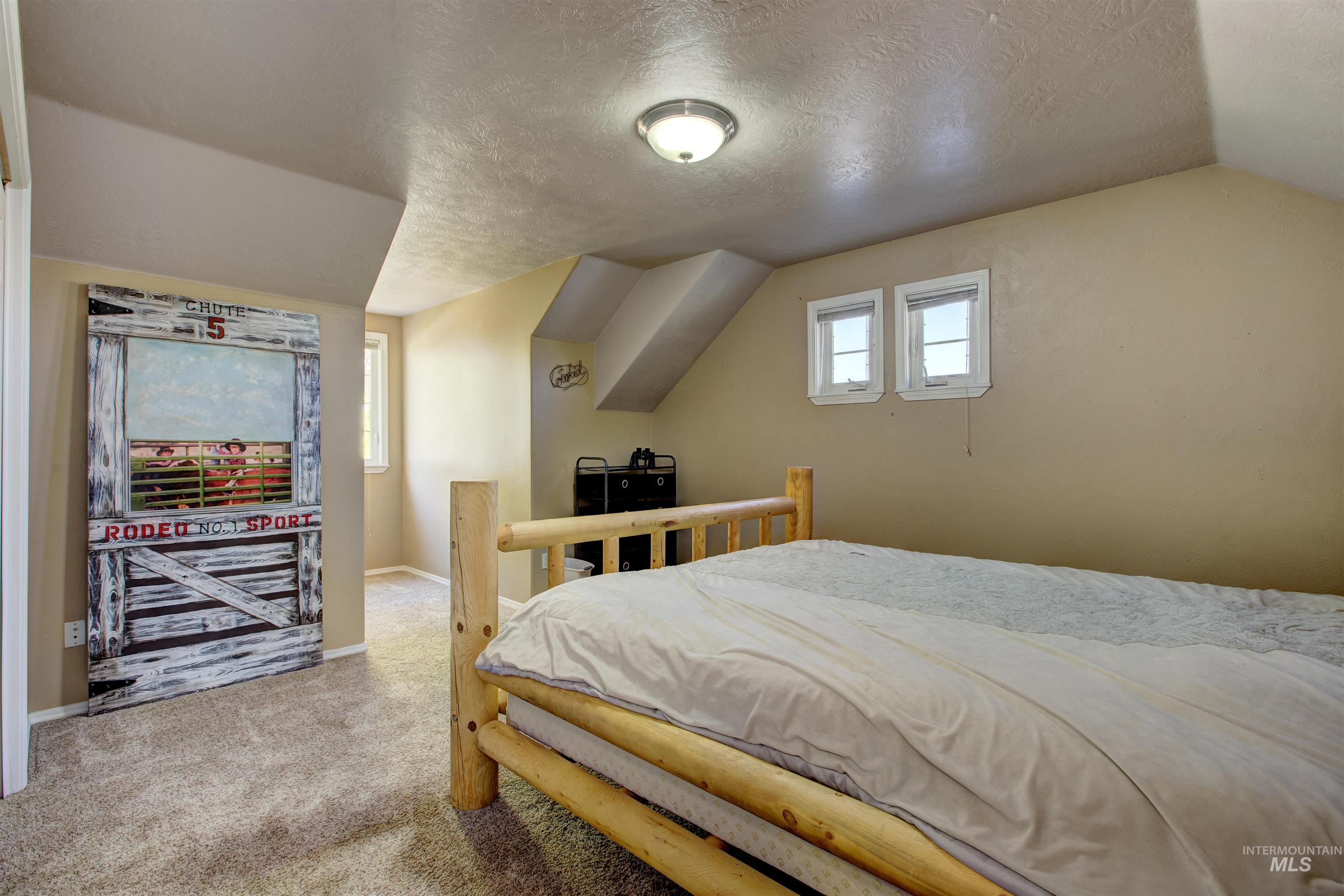 Bedroom with a textured ceiling, lofted ceiling, and light carpet