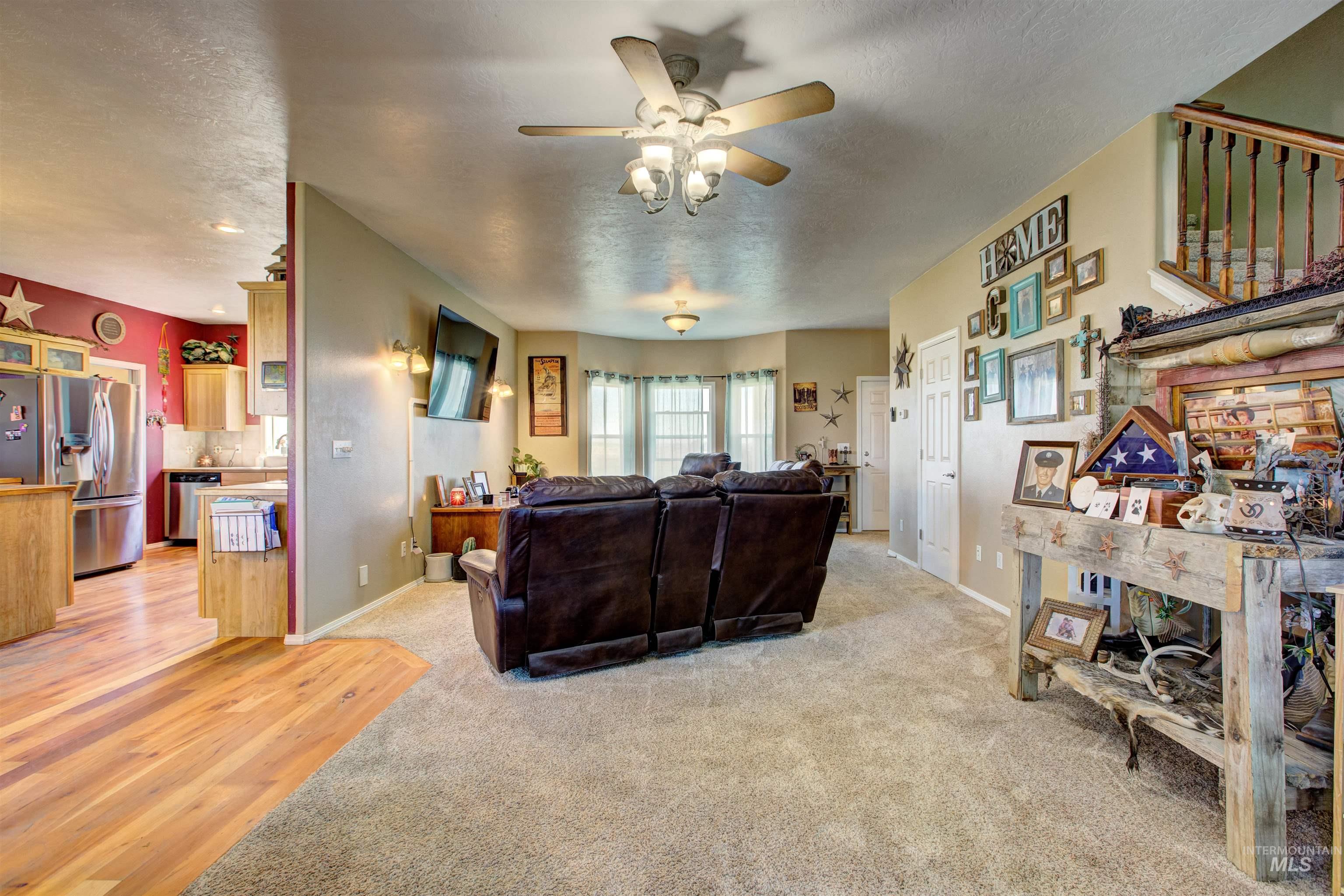 Living room featuring a textured ceiling, light wood-style flooring, light colored carpet, and a ceiling fan