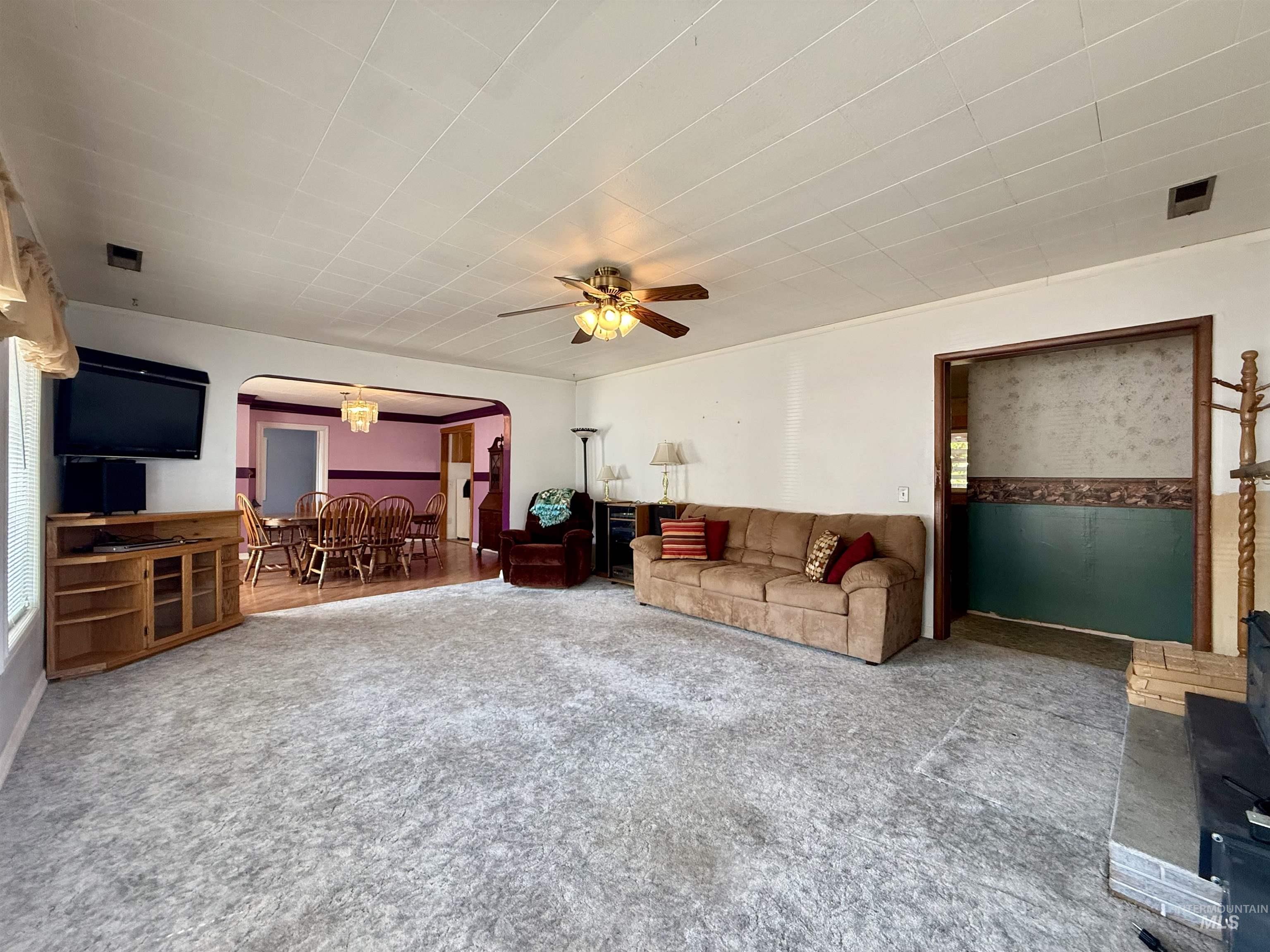Living room with arched walkways, carpet flooring, ceiling fan, and a chandelier