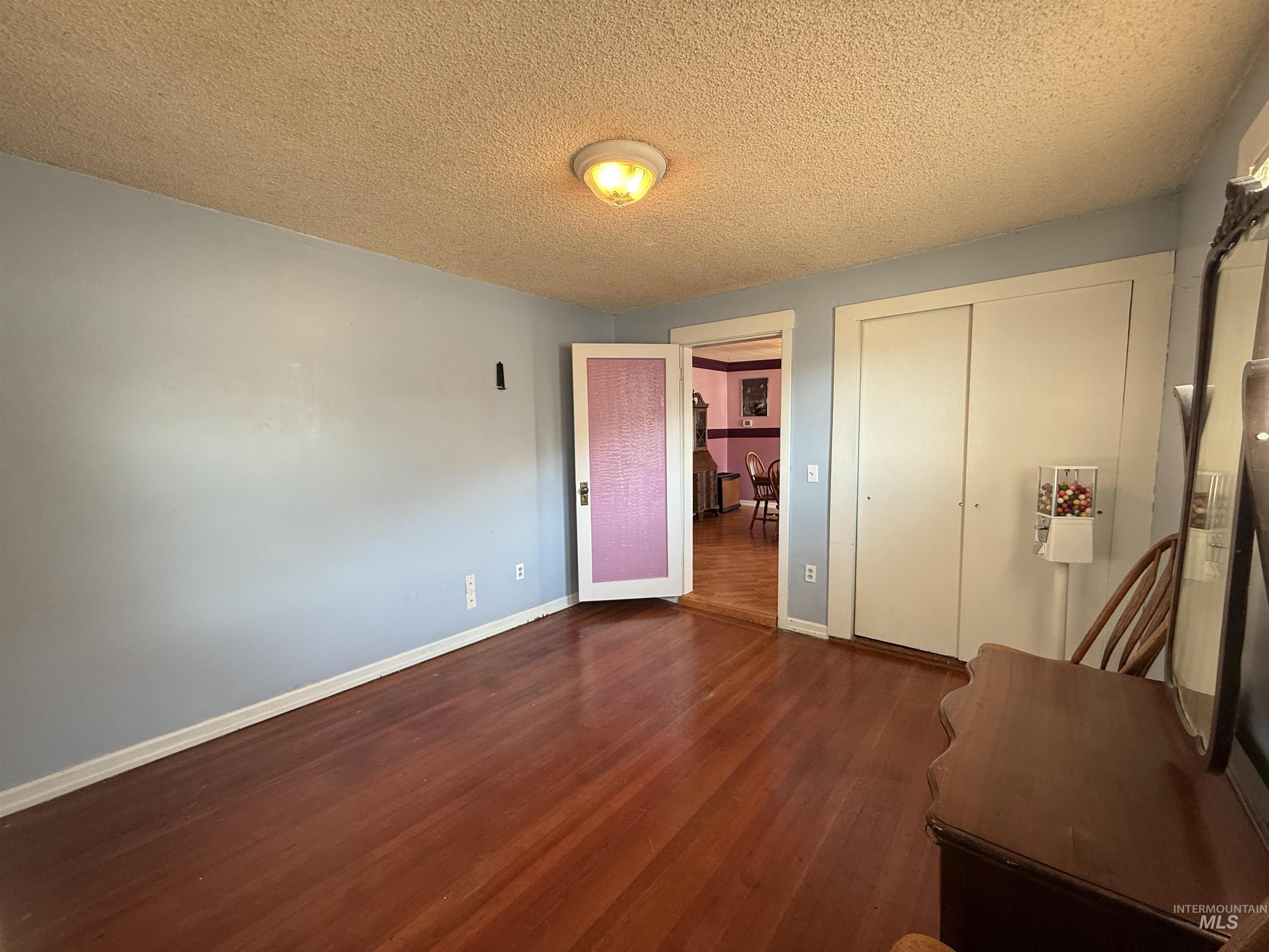 Unfurnished bedroom with a textured ceiling, dark wood-style flooring, and a closet