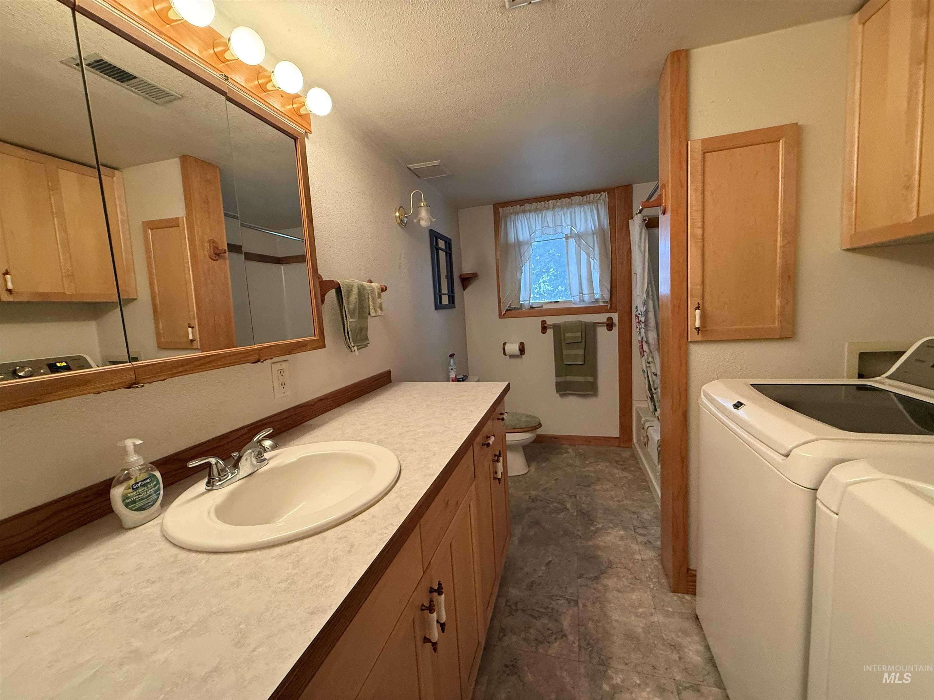 Bathroom featuring independent washer and dryer, a shower with shower curtain, a textured ceiling, vanity, and heating unit