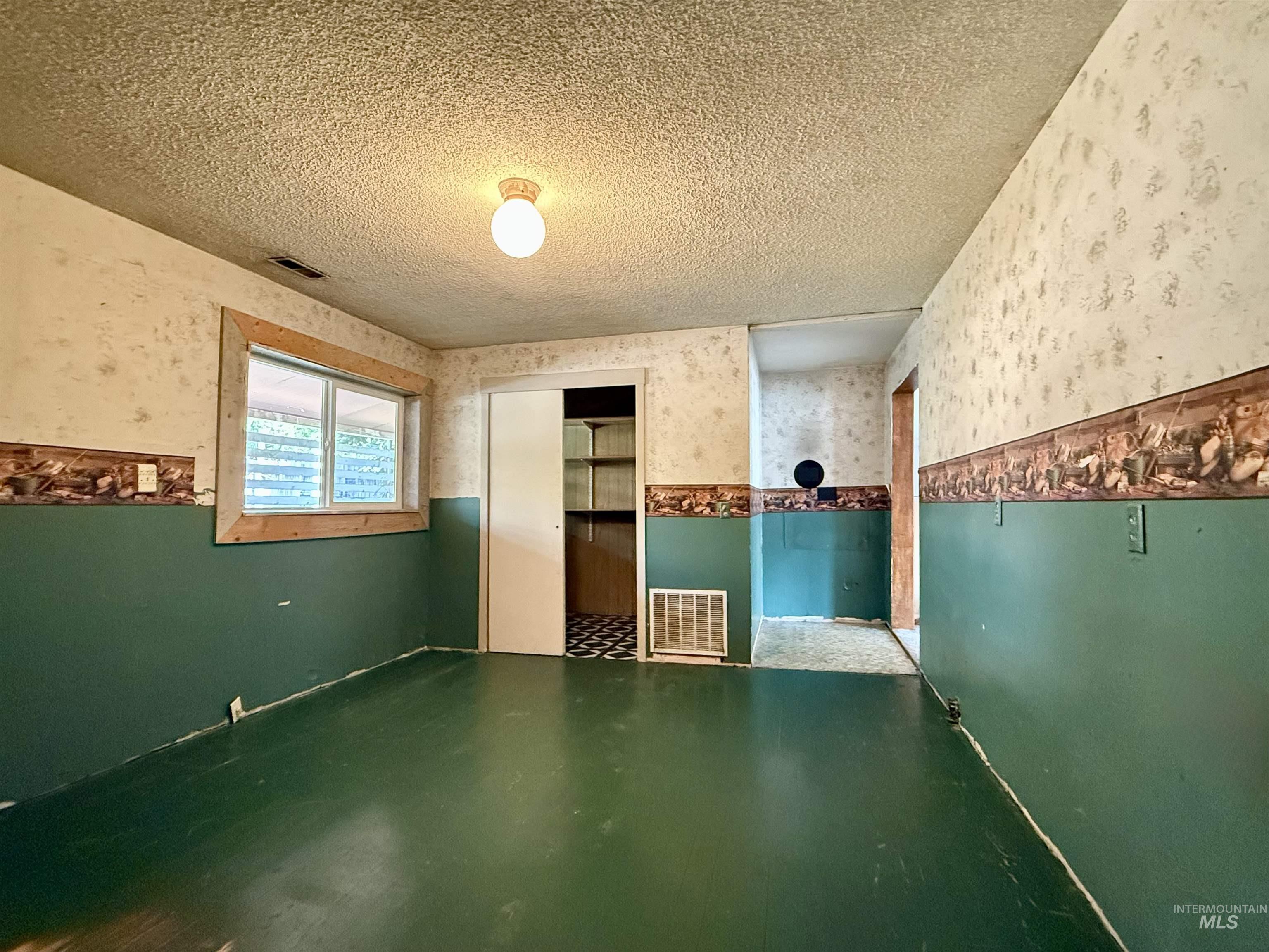 Misc room with wallpapered walls, a textured ceiling, and a wainscoted wall