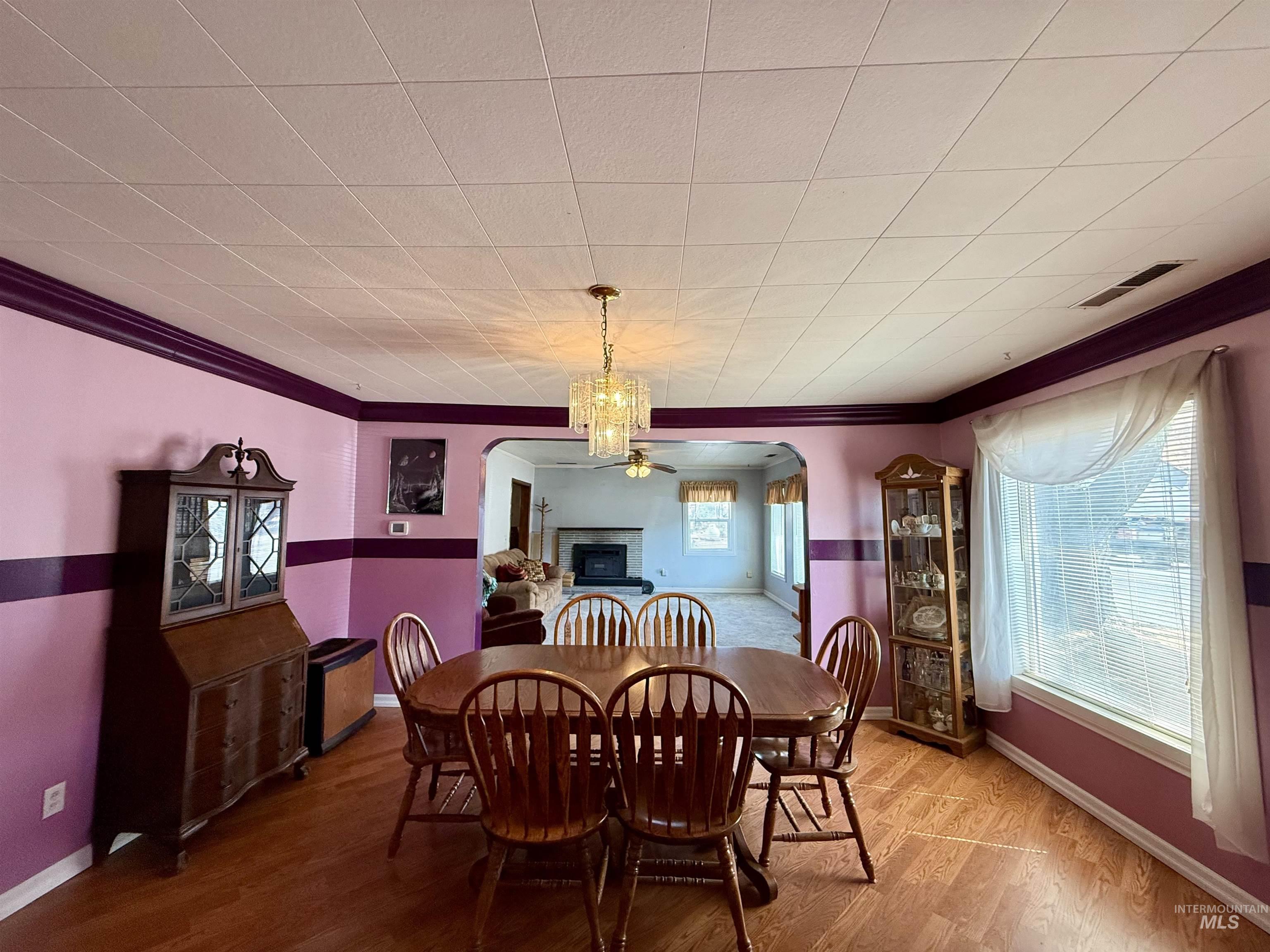 Dining area with crown molding, wood finished floors, arched walkways, and a fireplace