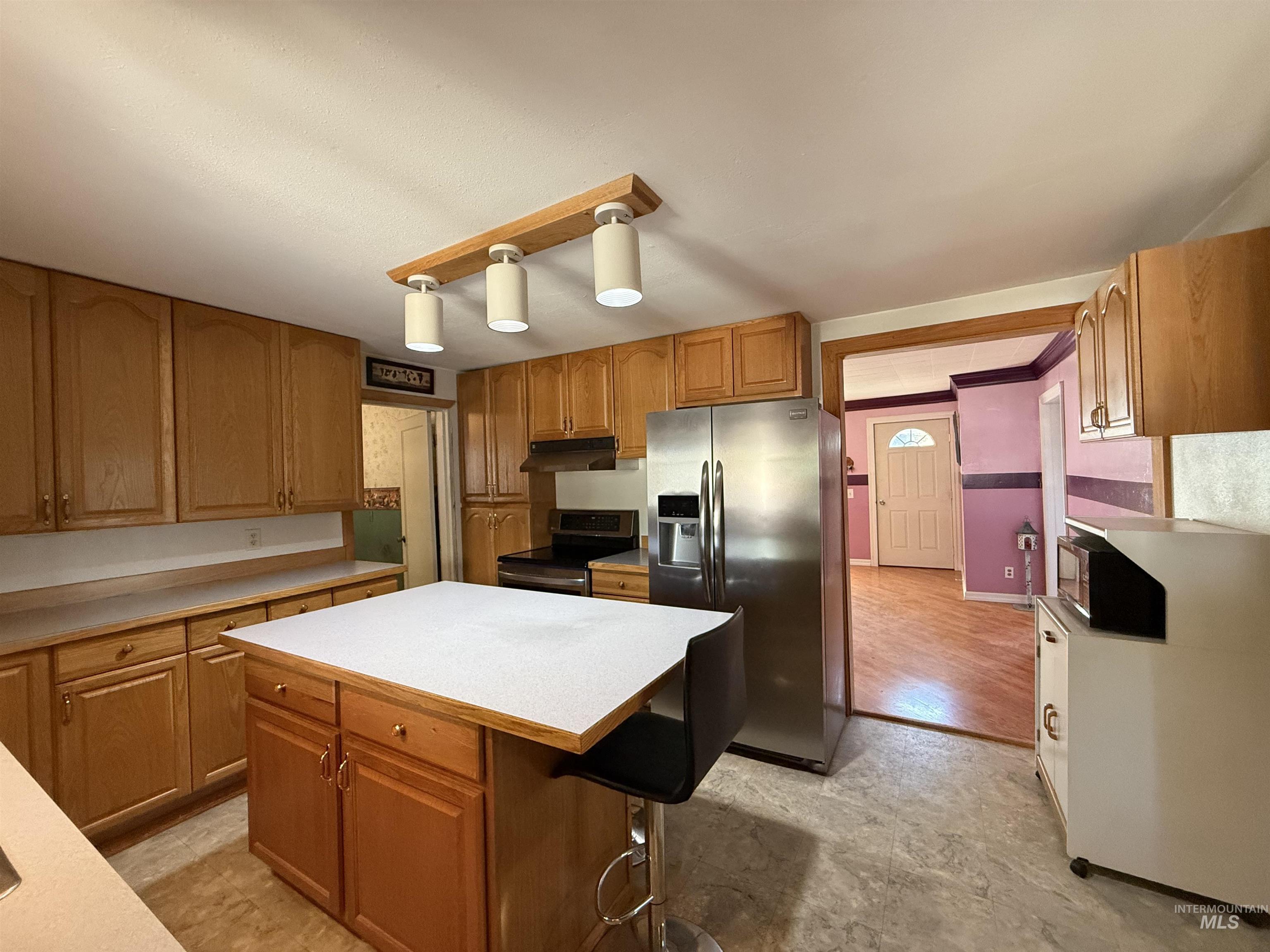 Kitchen with light countertops, stainless steel appliances, brown cabinetry, a kitchen breakfast bar, and a kitchen island