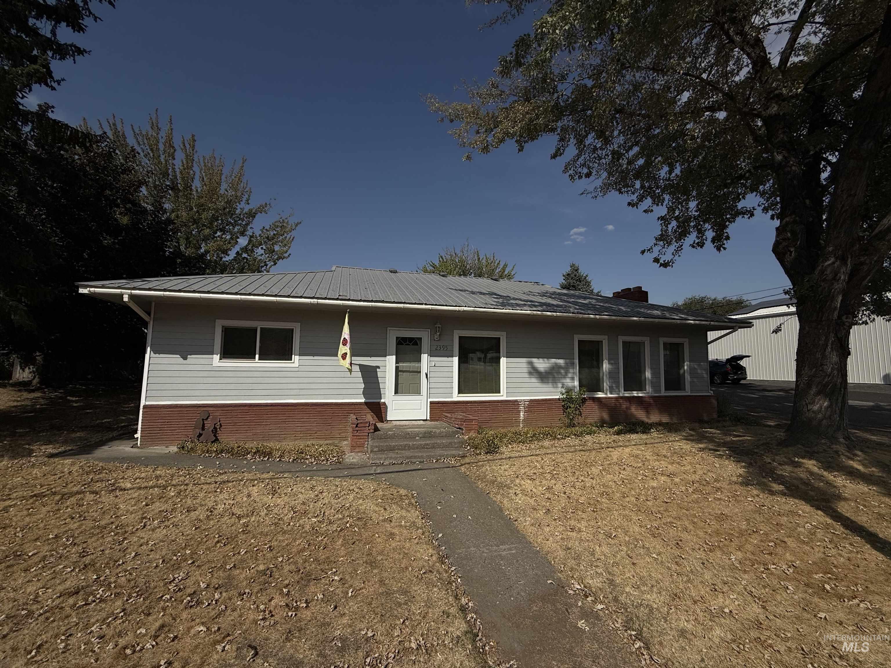View of front facade featuring brick siding, entry steps, a metal roof, and a chimney