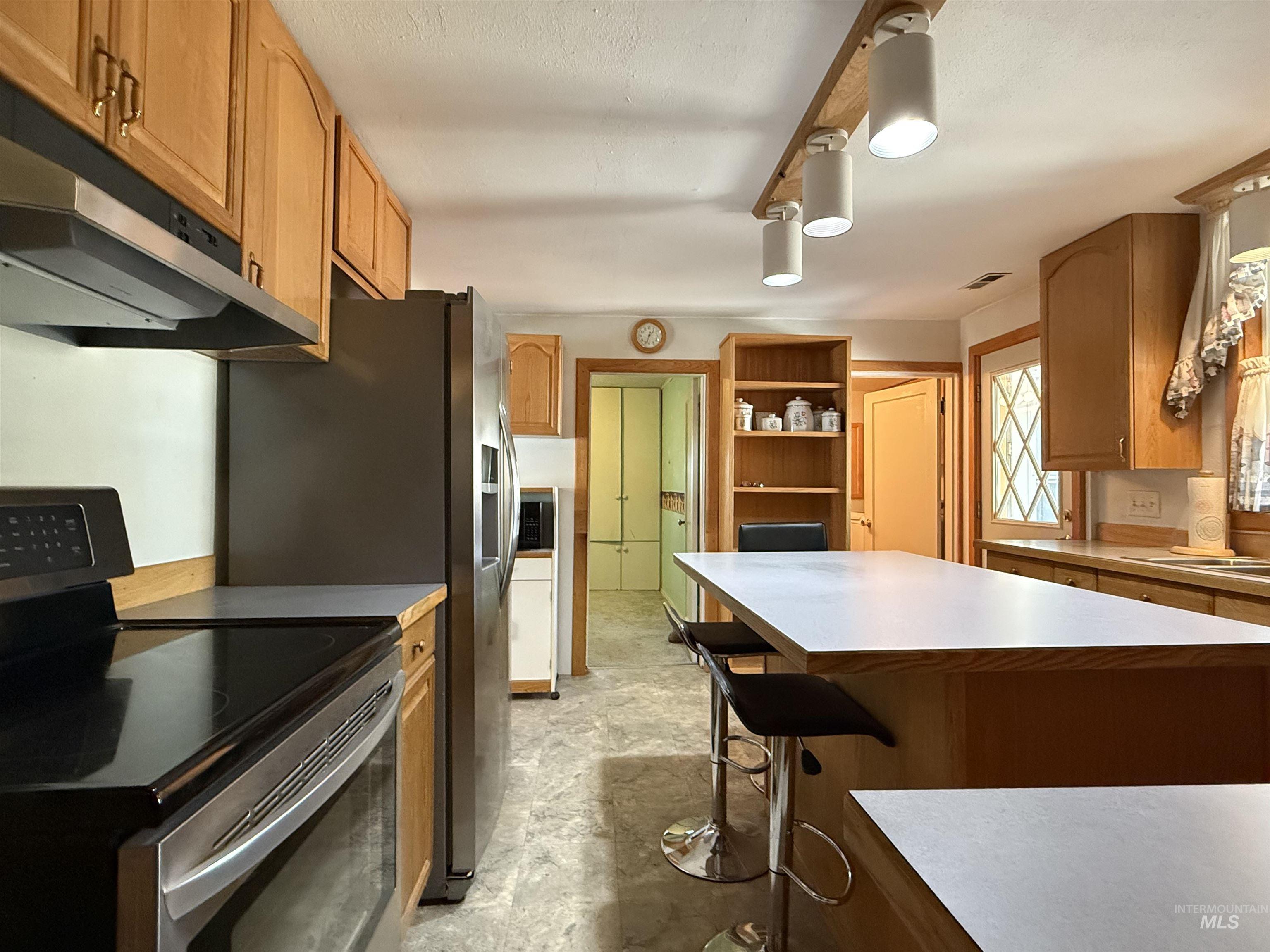 Kitchen with appliances with stainless steel finishes, light countertops, a breakfast bar, brown cabinets, and under cabinet range hood
