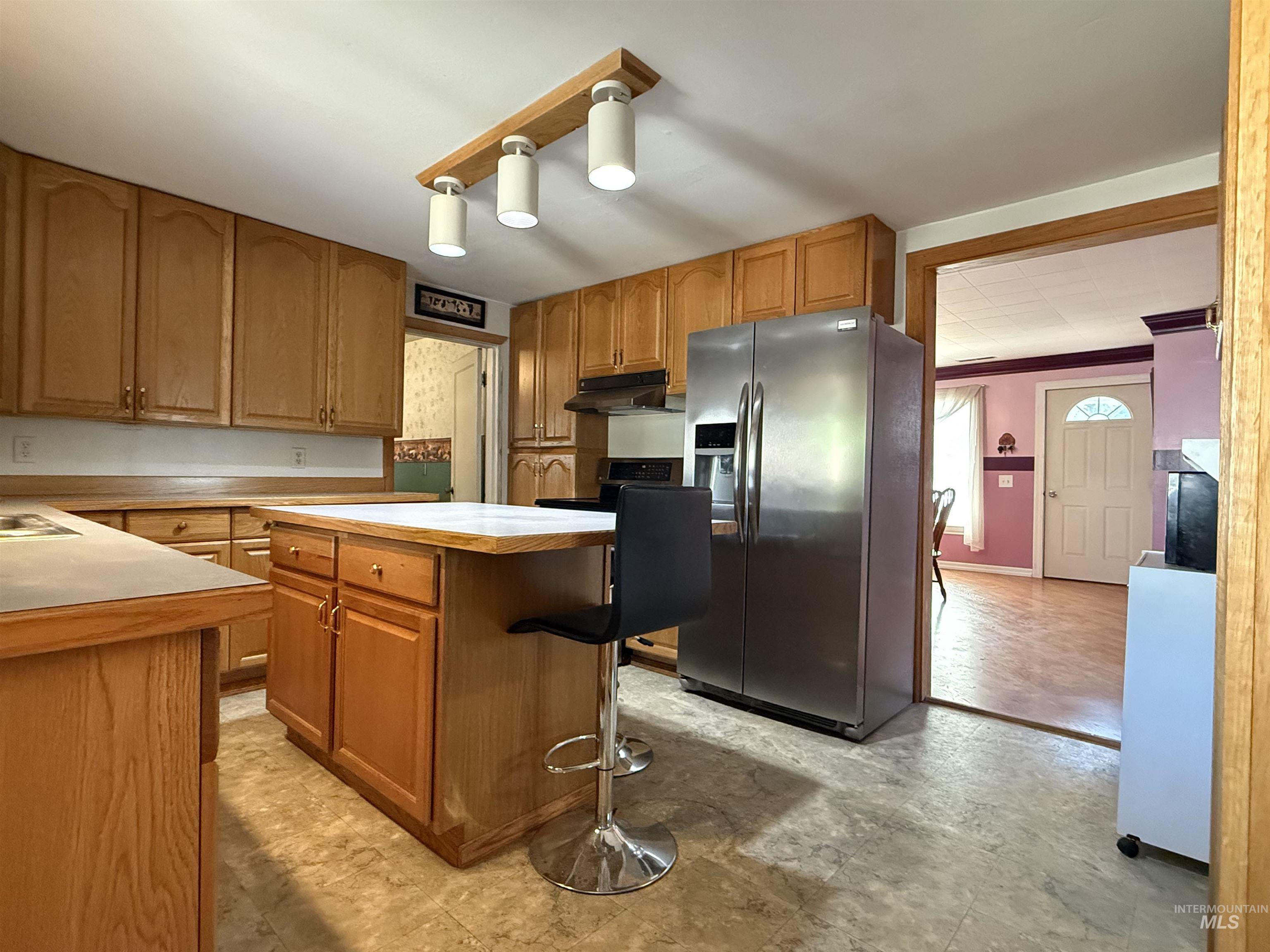 Kitchen with light countertops, appliances with stainless steel finishes, brown cabinetry, a center island, and a kitchen bar