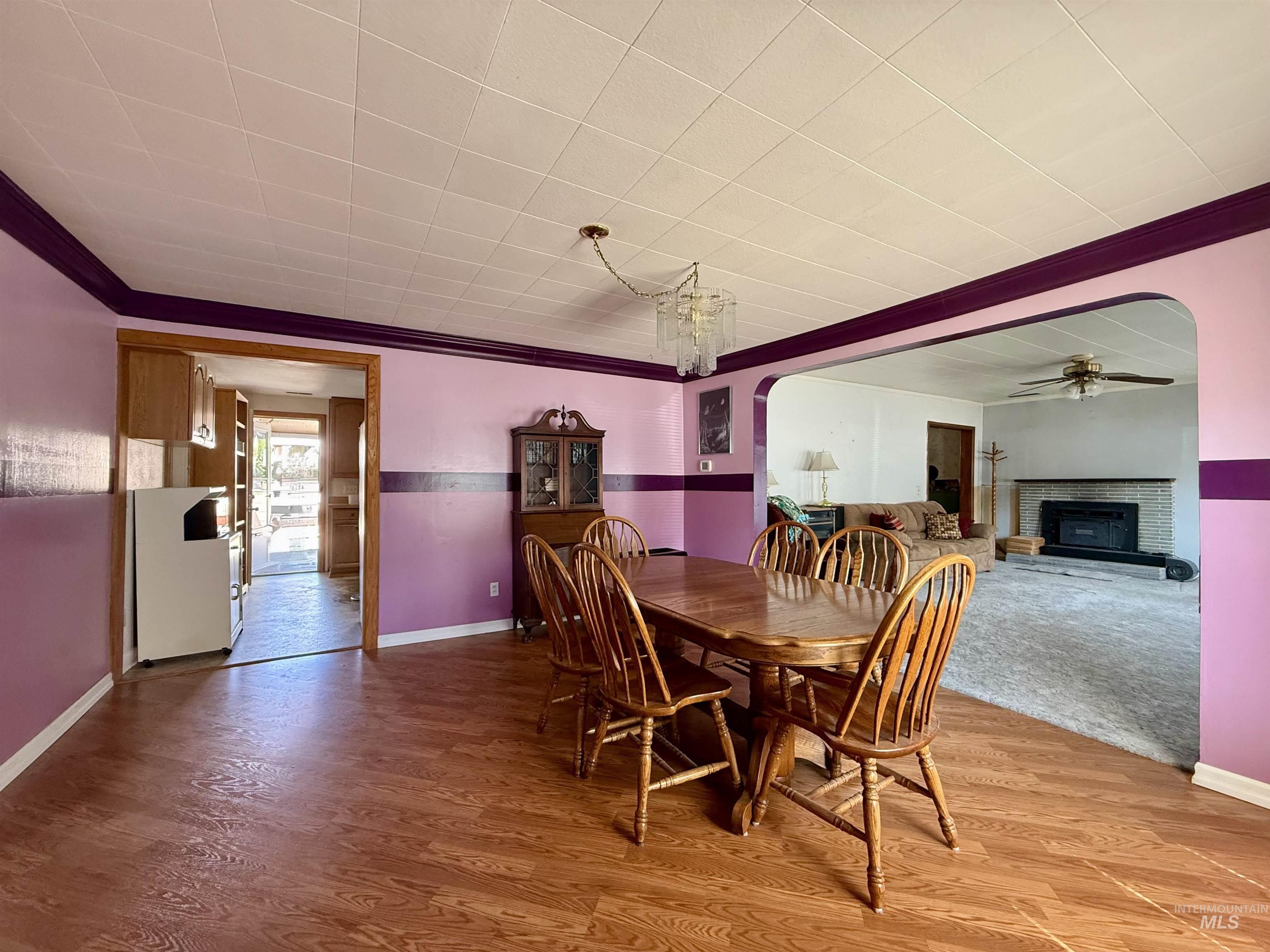 Dining room featuring arched walkways, a fireplace, wood finished floors, crown molding, and a chandelier
