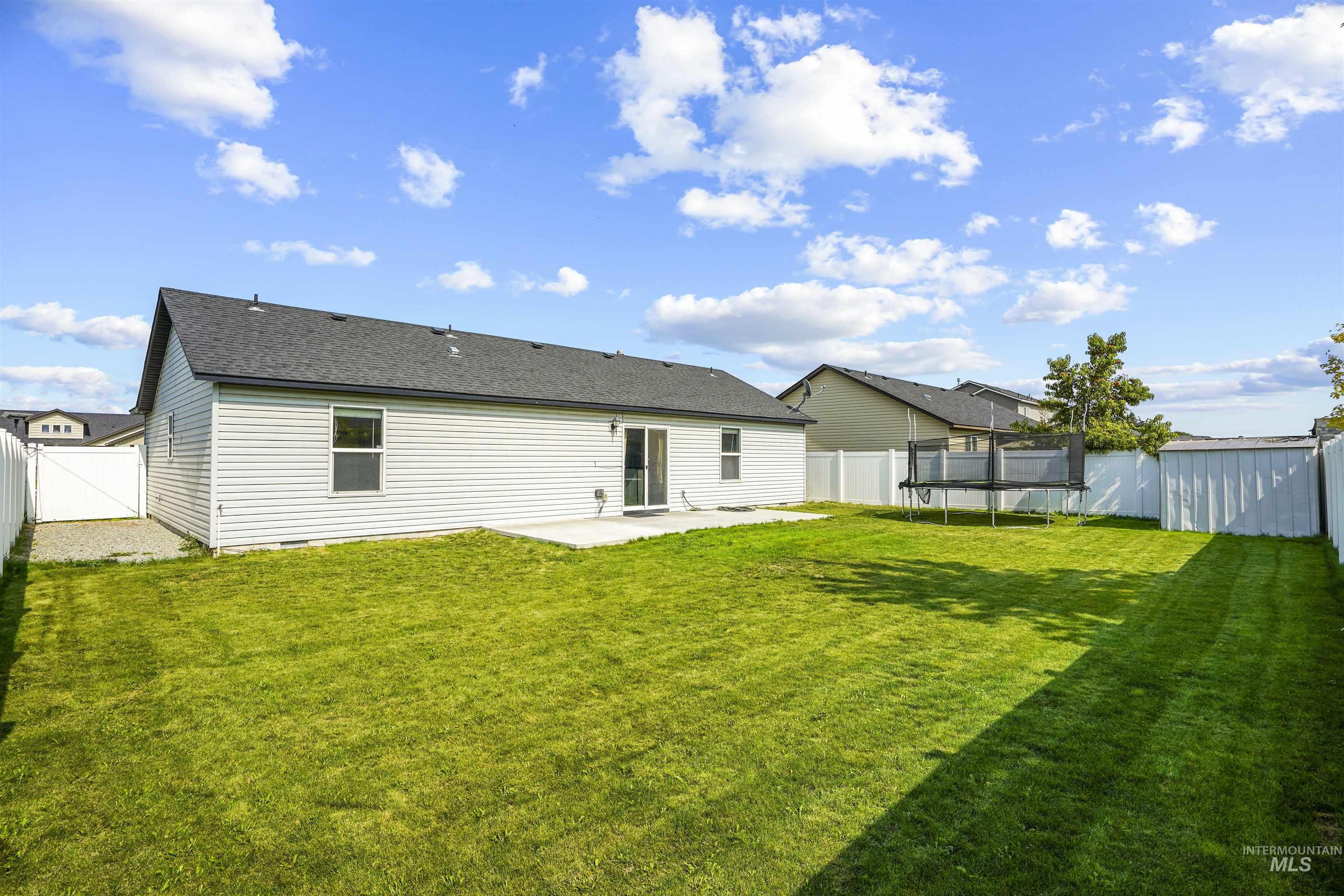 Rear view of house with a patio area, a trampoline, a fenced backyard, and roof with shingles