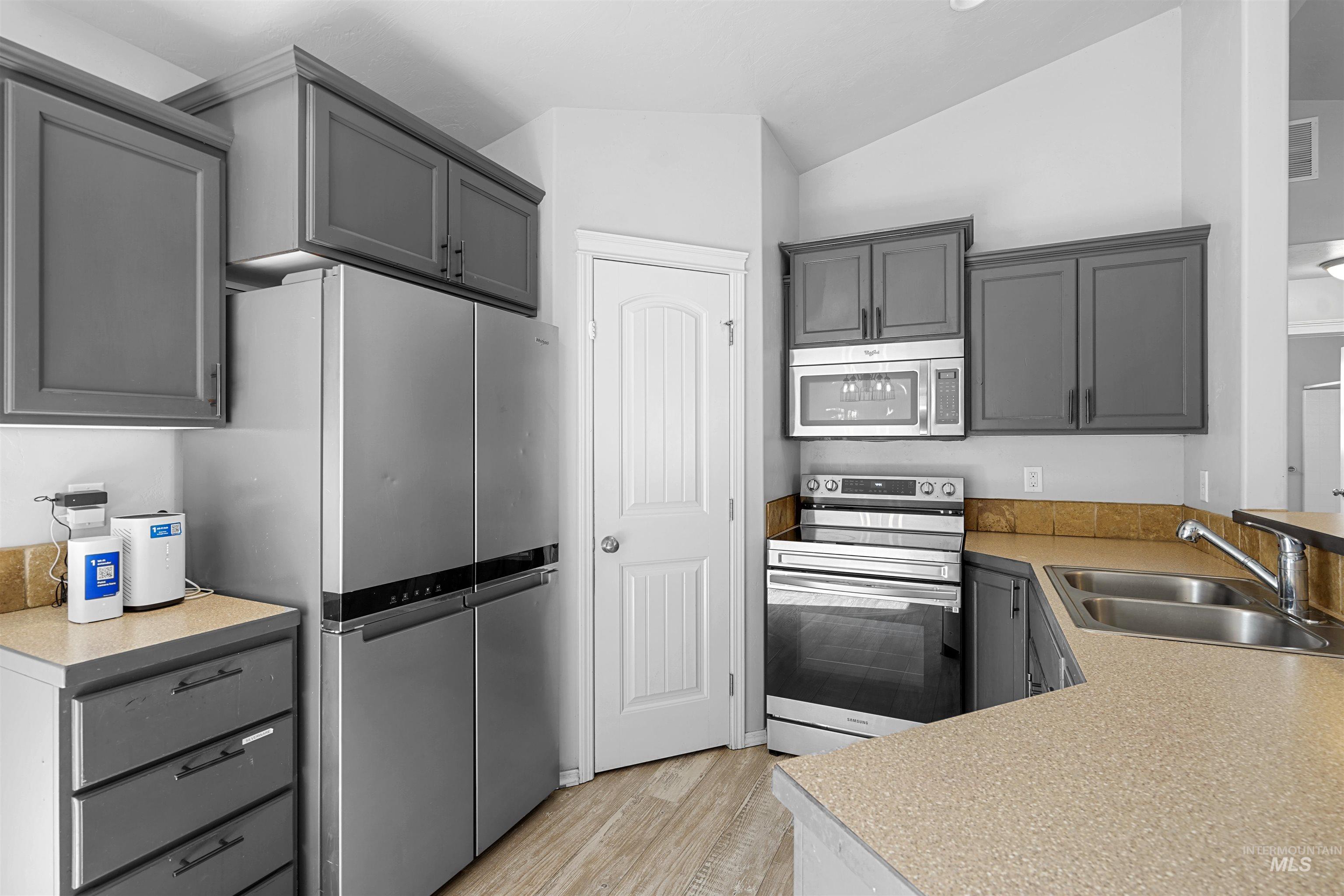 Kitchen with appliances with stainless steel finishes, gray cabinetry, light wood finished floors, light countertops, and lofted ceiling
