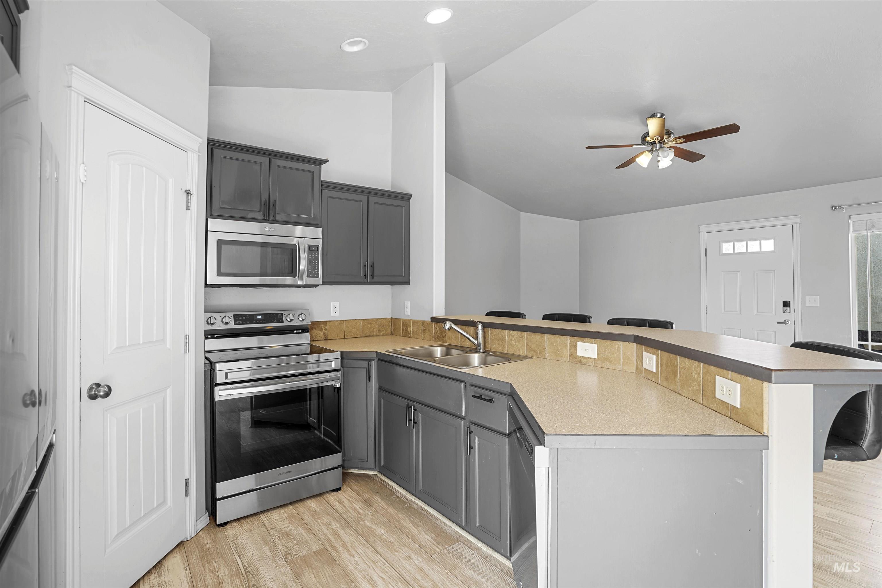 Kitchen with appliances with stainless steel finishes, lofted ceiling, a peninsula, a kitchen breakfast bar, and light wood-style floors