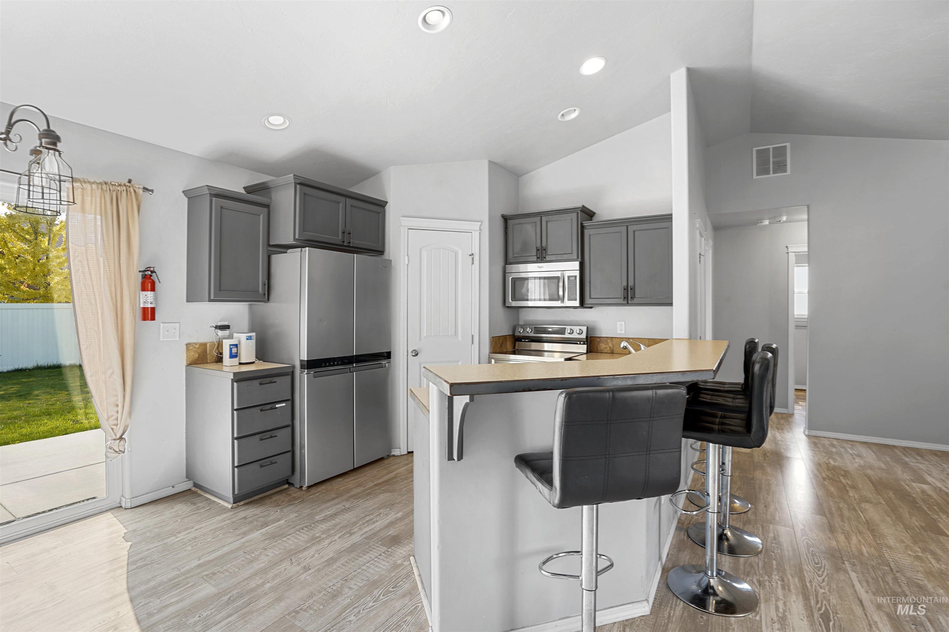 Kitchen featuring vaulted ceiling, appliances with stainless steel finishes, a kitchen breakfast bar, light wood finished floors, and gray cabinetry