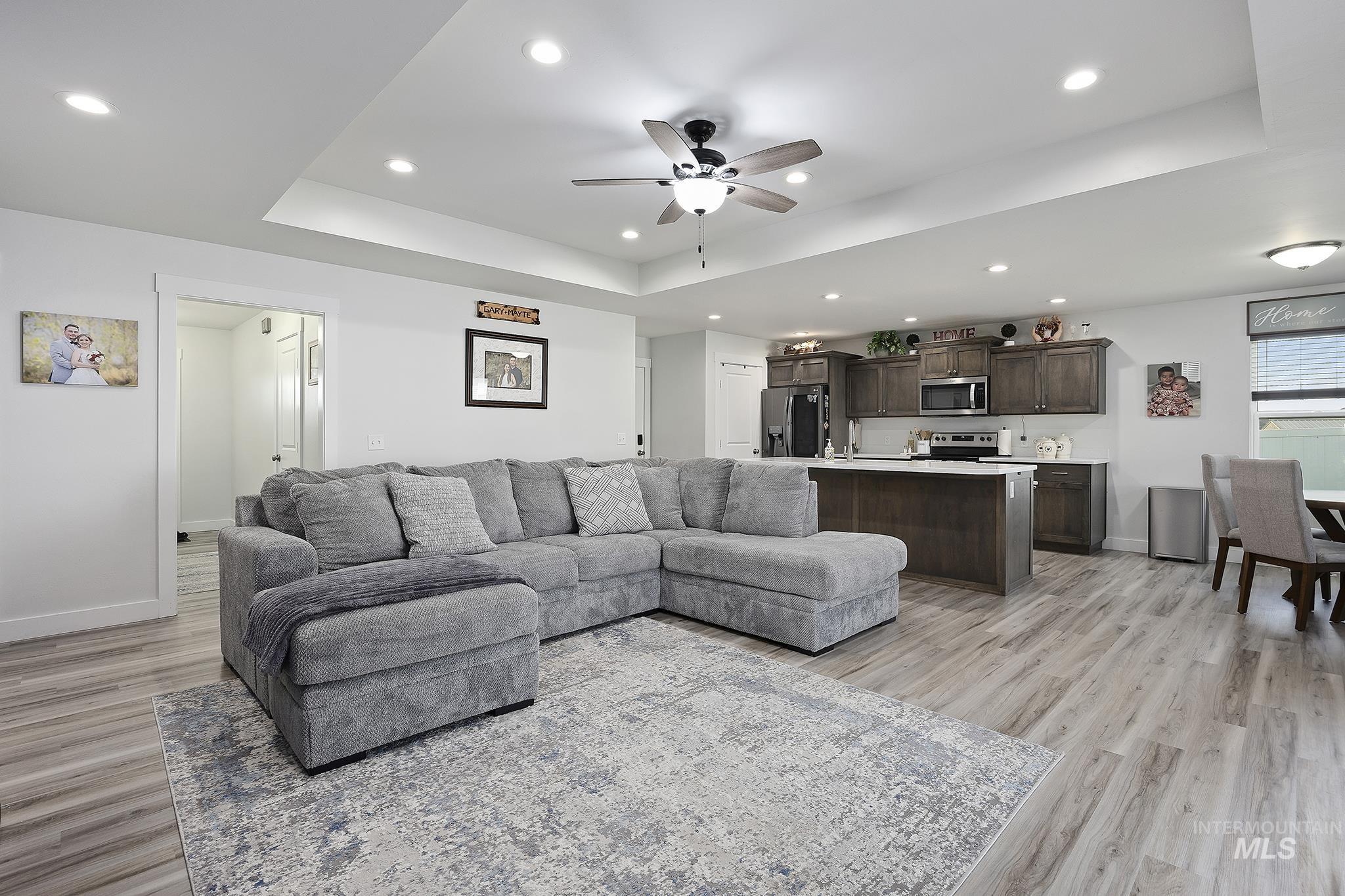 Living room with a raised ceiling, a ceiling fan, recessed lighting, and light wood-type flooring