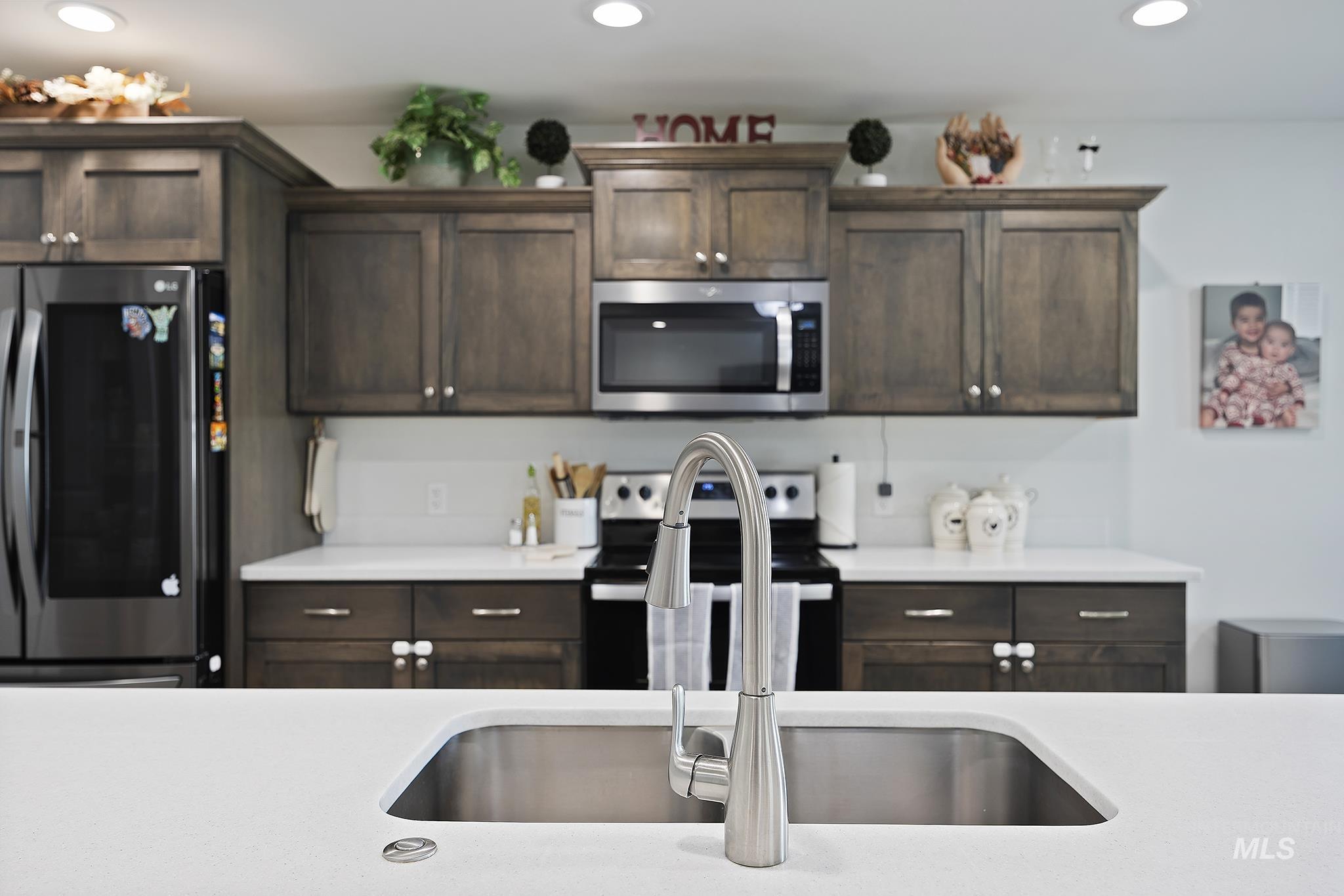 Kitchen with dark brown cabinetry, appliances with stainless steel finishes, recessed lighting, and light stone countertops