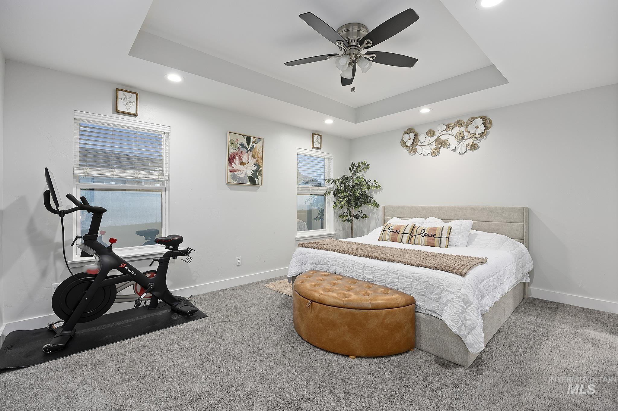 Carpeted bedroom featuring a raised ceiling, ceiling fan, and recessed lighting