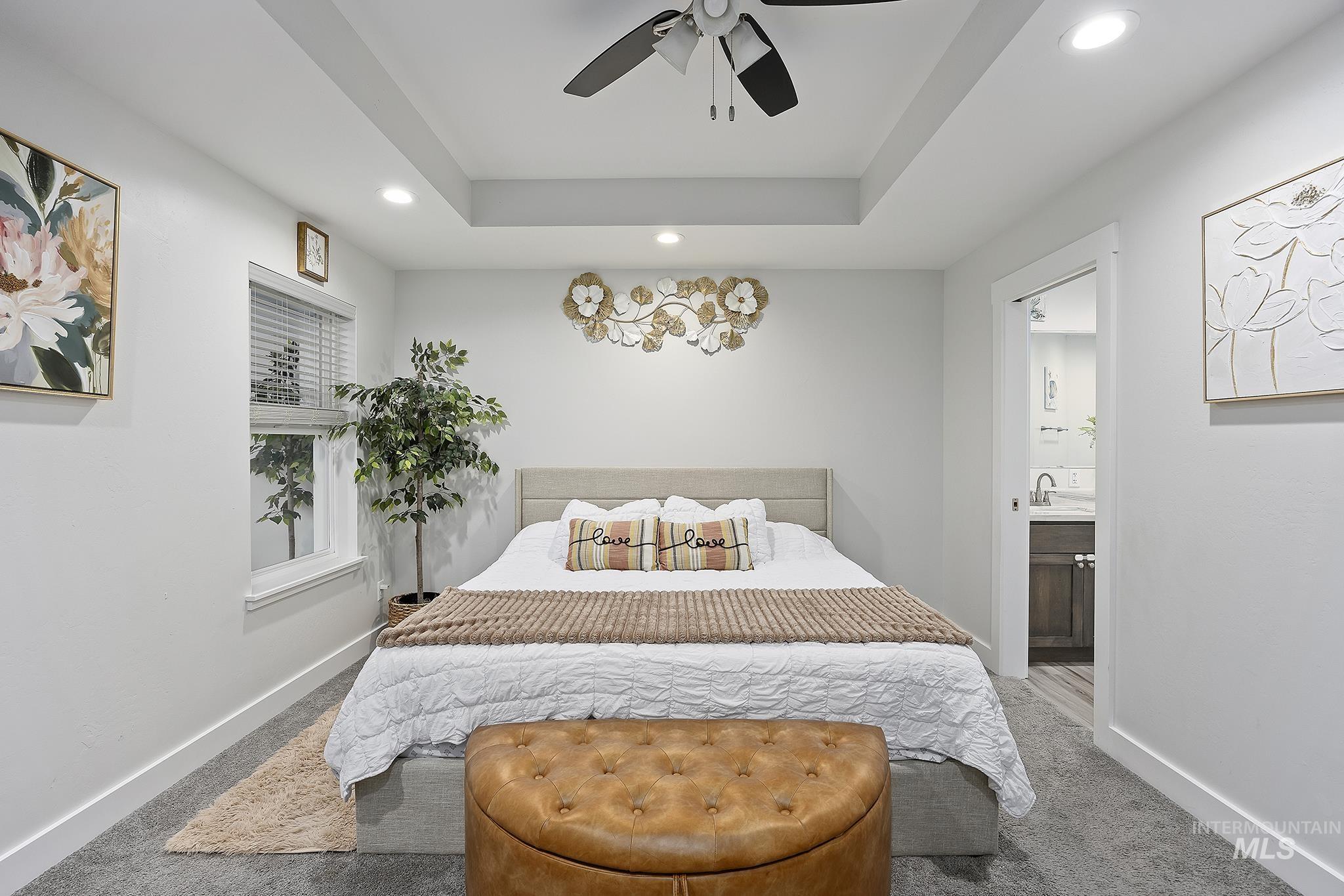 Carpeted bedroom featuring connected bathroom, recessed lighting, a tray ceiling, and a ceiling fan