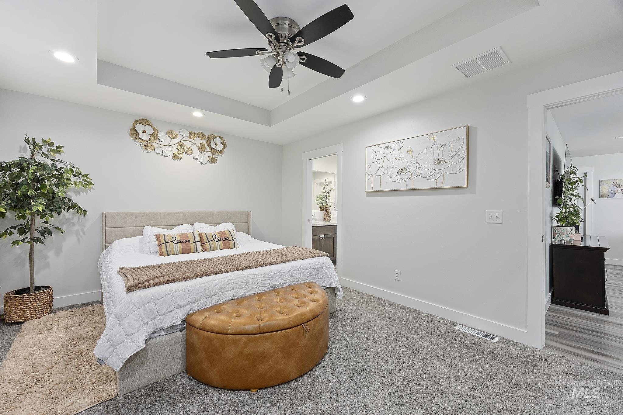 Bedroom with a tray ceiling, carpet floors, recessed lighting, ceiling fan, and ensuite bathroom