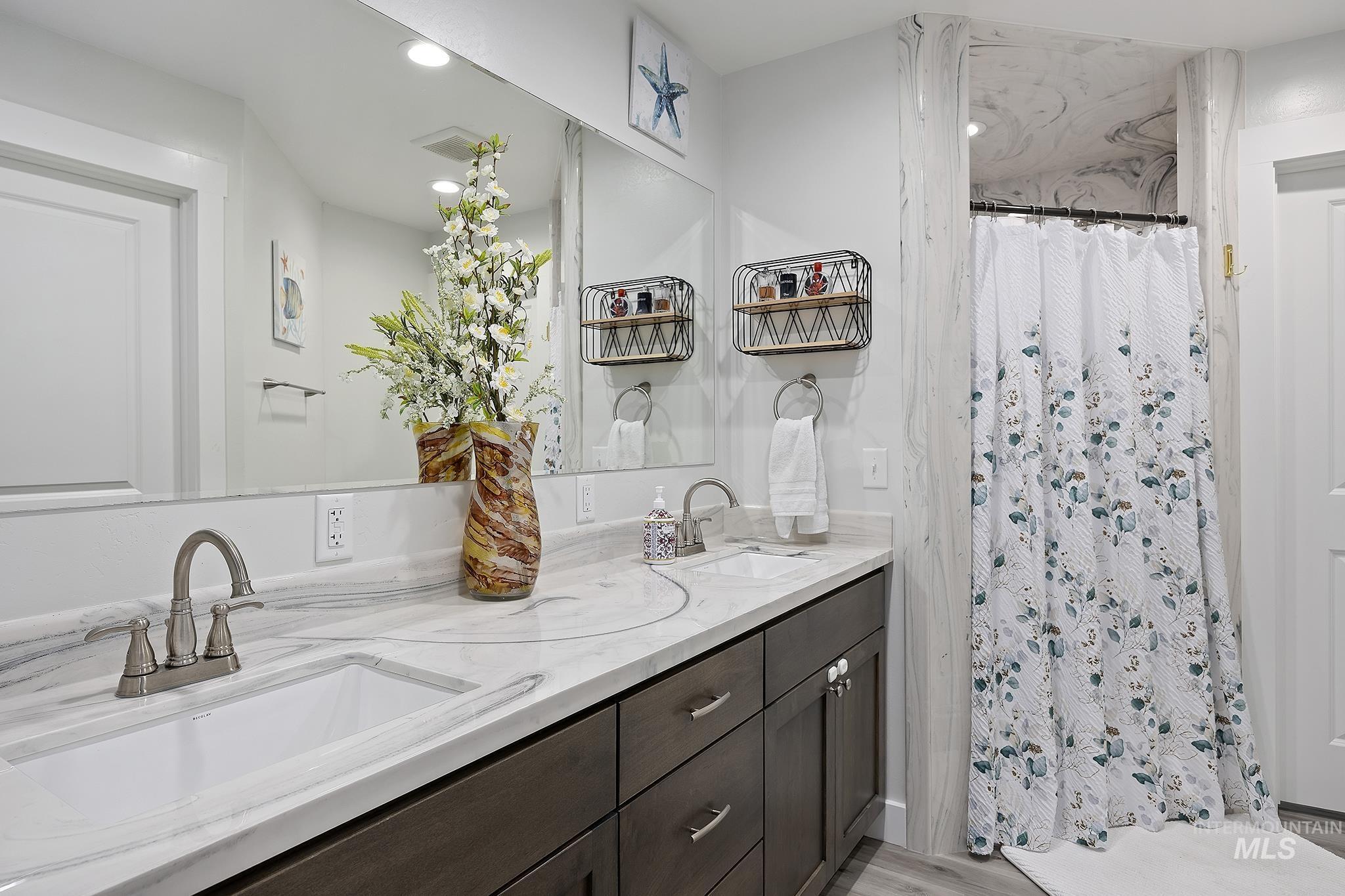 Full bath featuring double vanity, a shower stall, light wood-type flooring, and recessed lighting