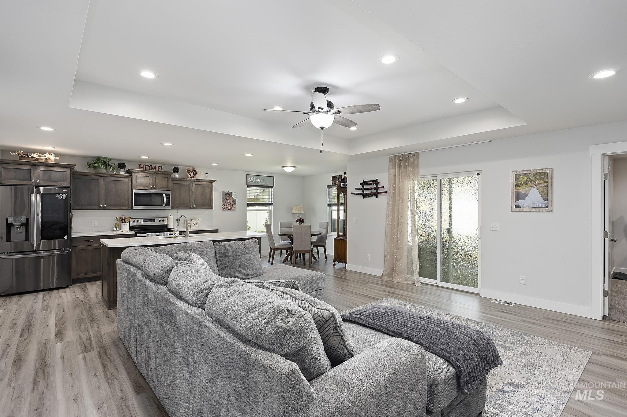 Living room with a tray ceiling, recessed lighting, light wood-style flooring, and a ceiling fan