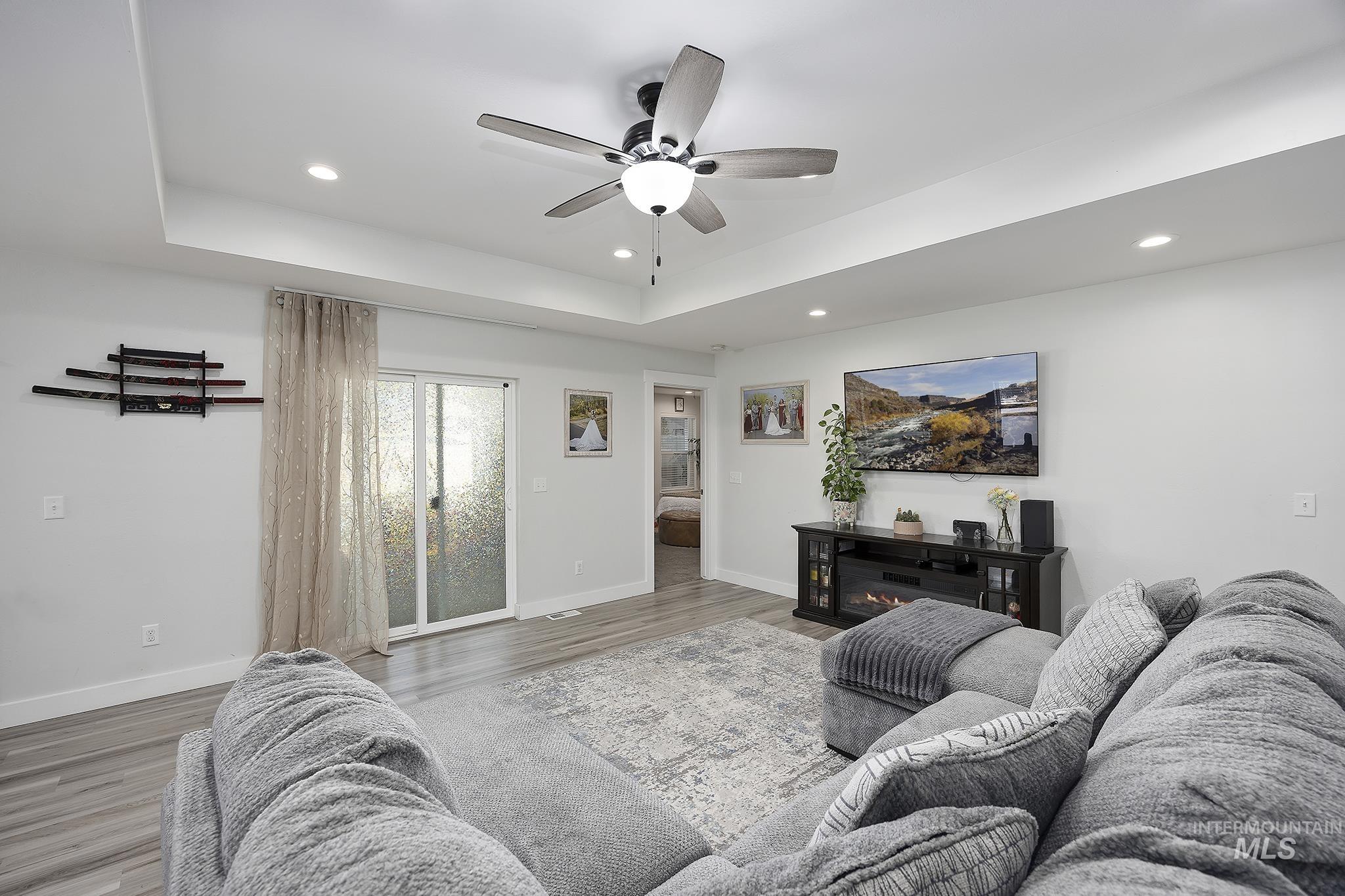 Living area featuring wood finished floors, recessed lighting, ceiling fan, a tray ceiling, and a glass covered fireplace