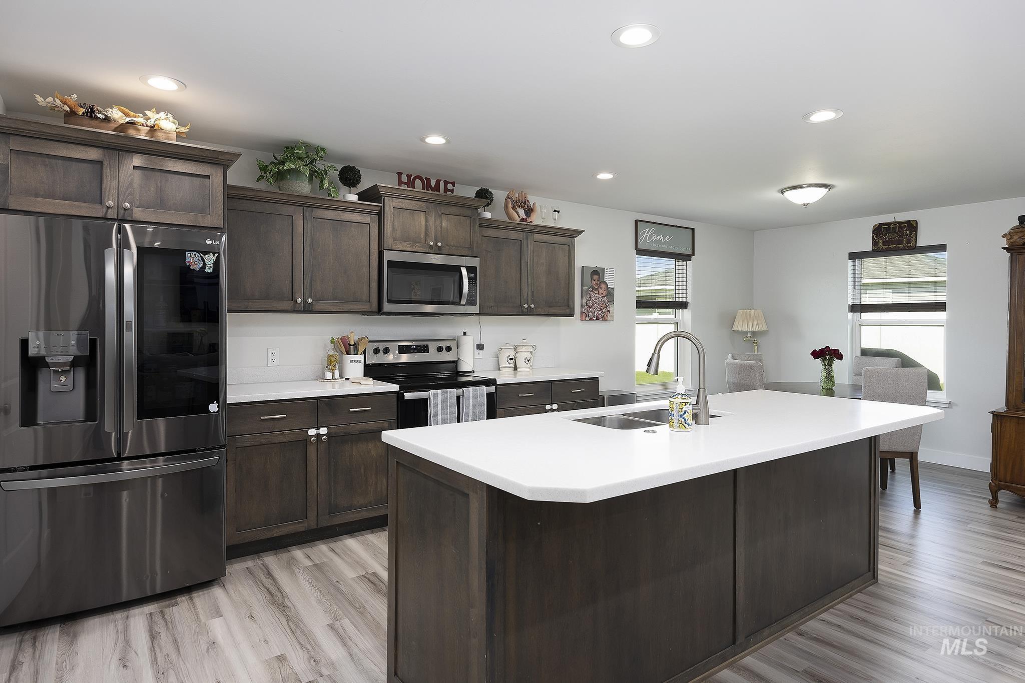 Kitchen with stainless steel appliances, dark brown cabinets, recessed lighting, light wood-style flooring, and a center island with sink