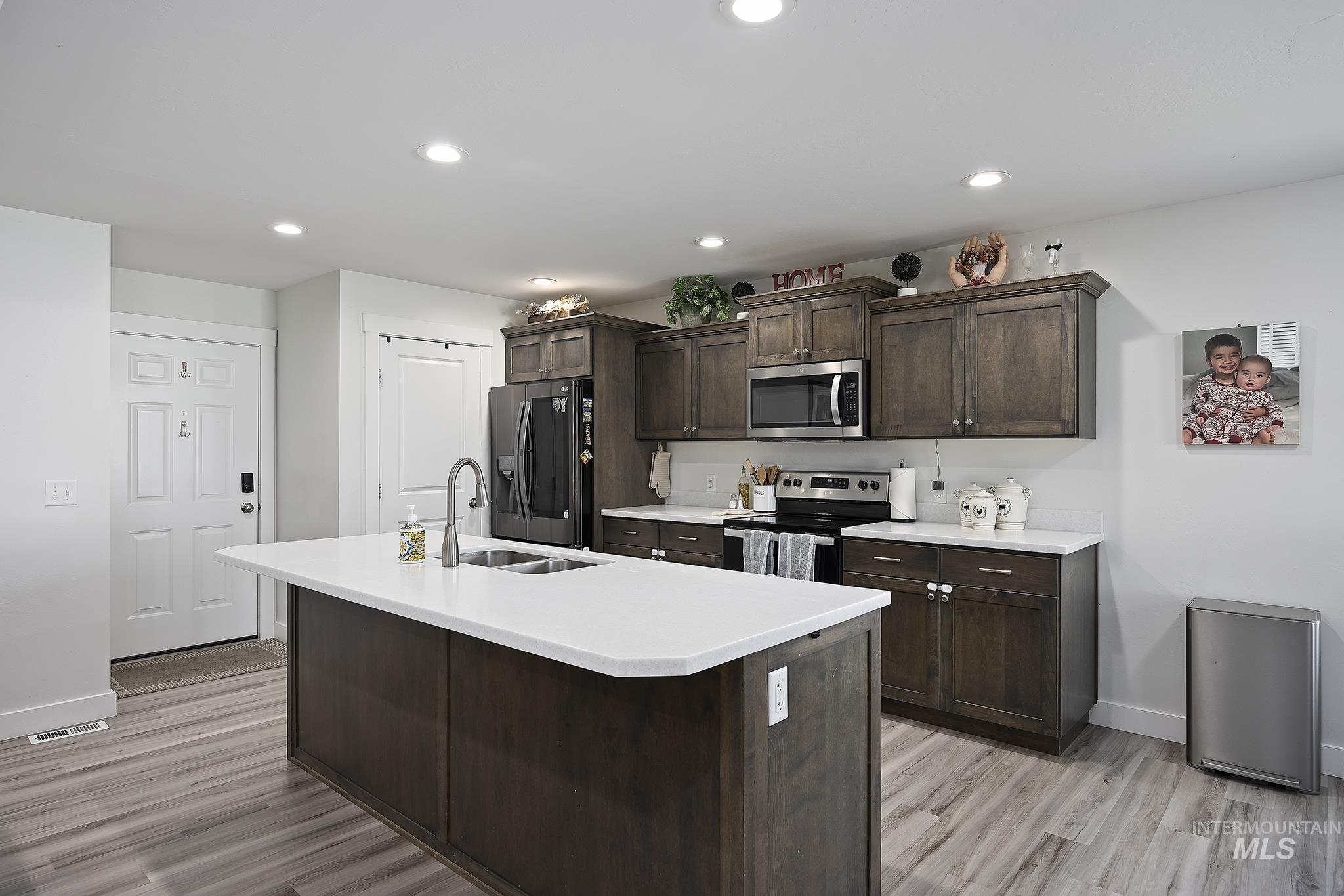 Kitchen featuring dark brown cabinets, appliances with stainless steel finishes, a center island with sink, recessed lighting, and light wood-type flooring