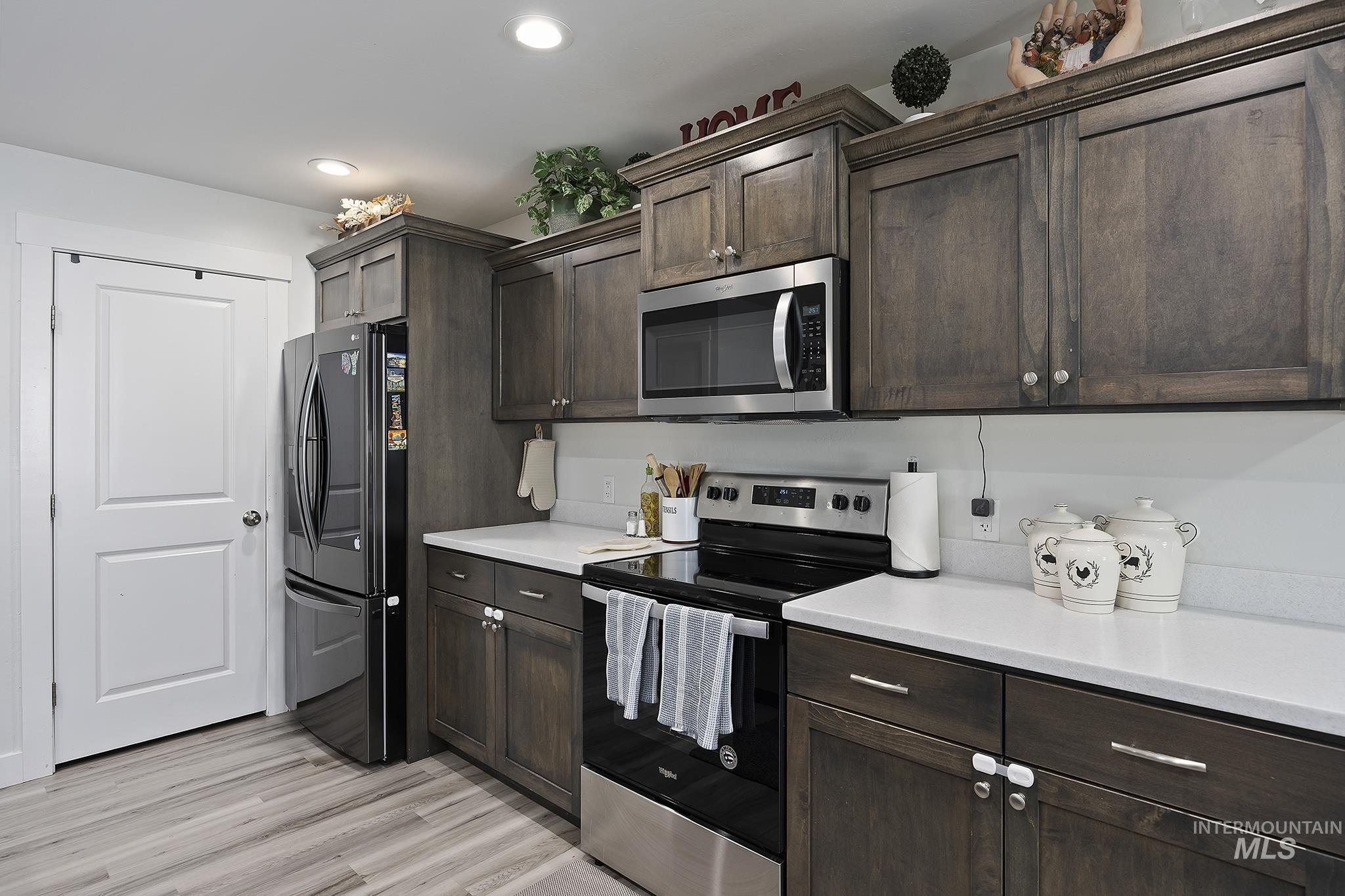 Kitchen featuring appliances with stainless steel finishes, dark brown cabinets, light wood-style flooring, and recessed lighting