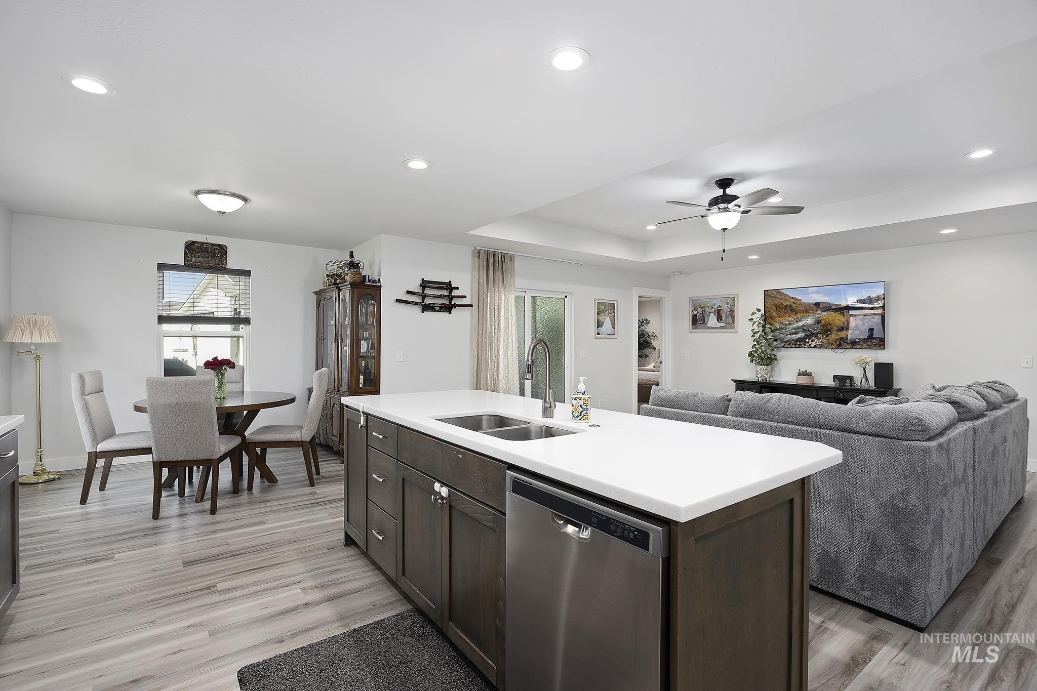 Kitchen with stainless steel dishwasher, recessed lighting, dark brown cabinetry, a kitchen island with sink, and a raised ceiling