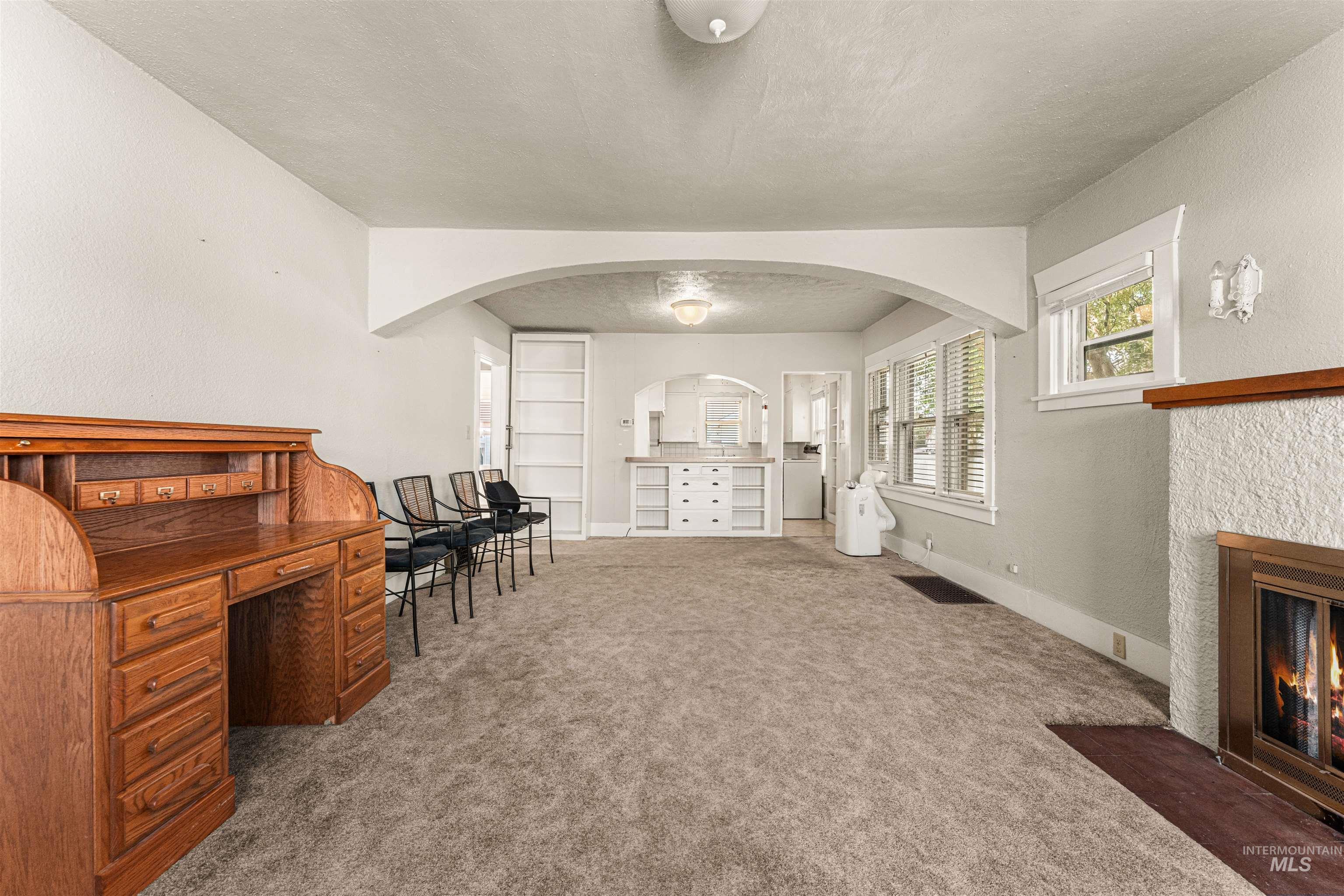 Living area featuring carpet, a textured ceiling, a fireplace with flush hearth, an office area, and arched walkways