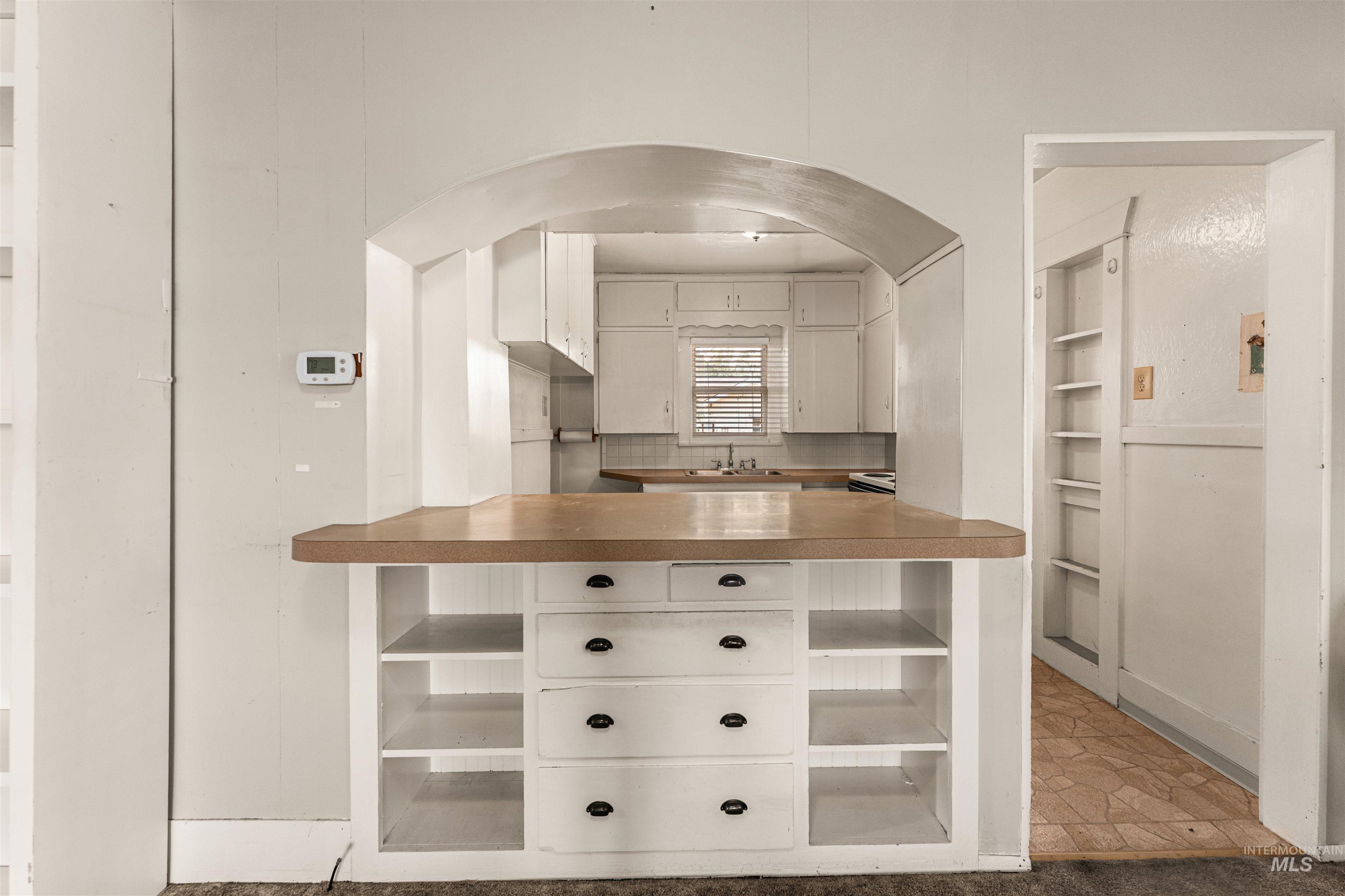 Kitchen featuring white cabinetry, open shelves, decorative backsplash, and light countertops