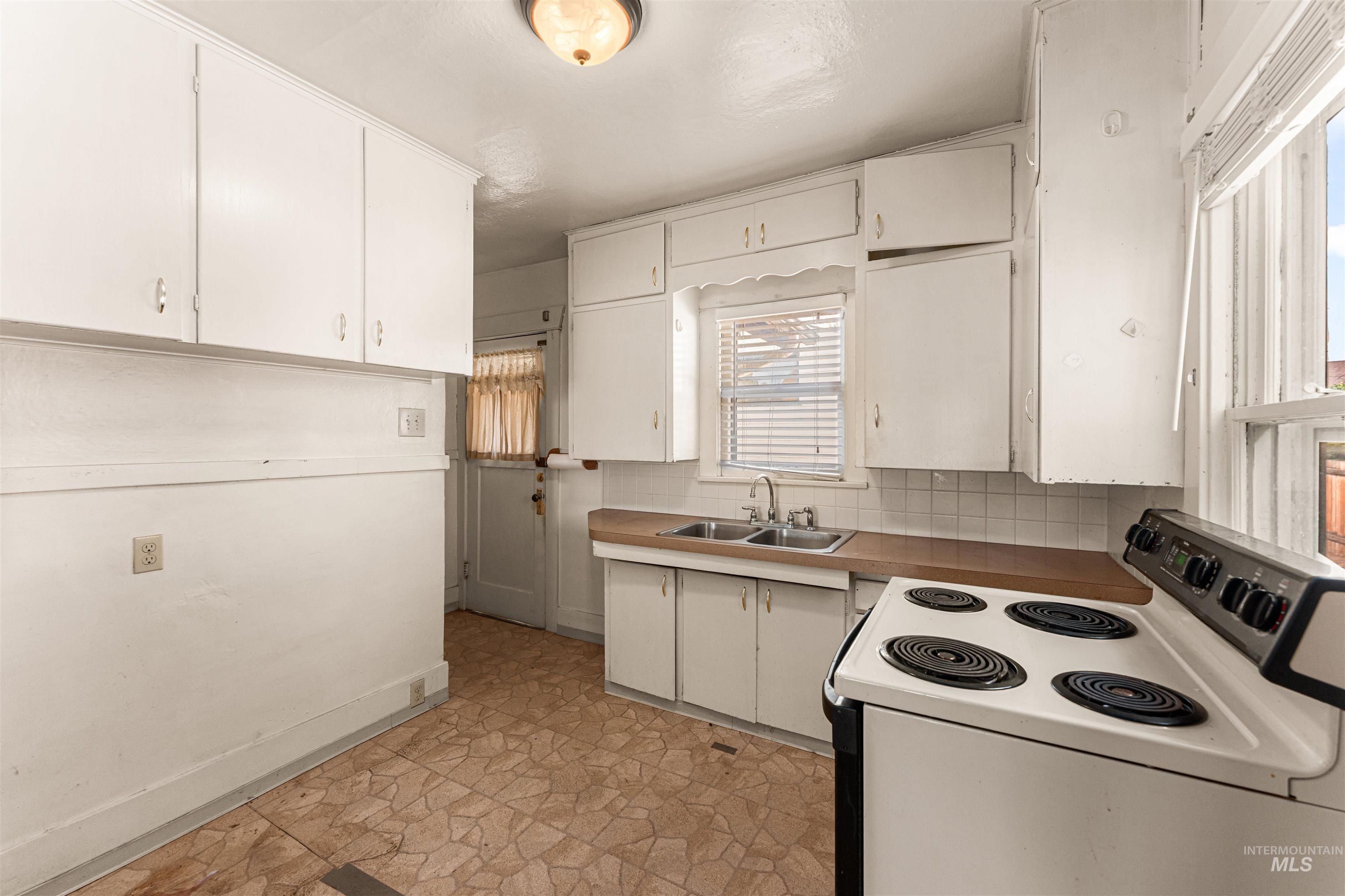 Kitchen featuring white range with electric cooktop, tasteful backsplash, and white cabinets