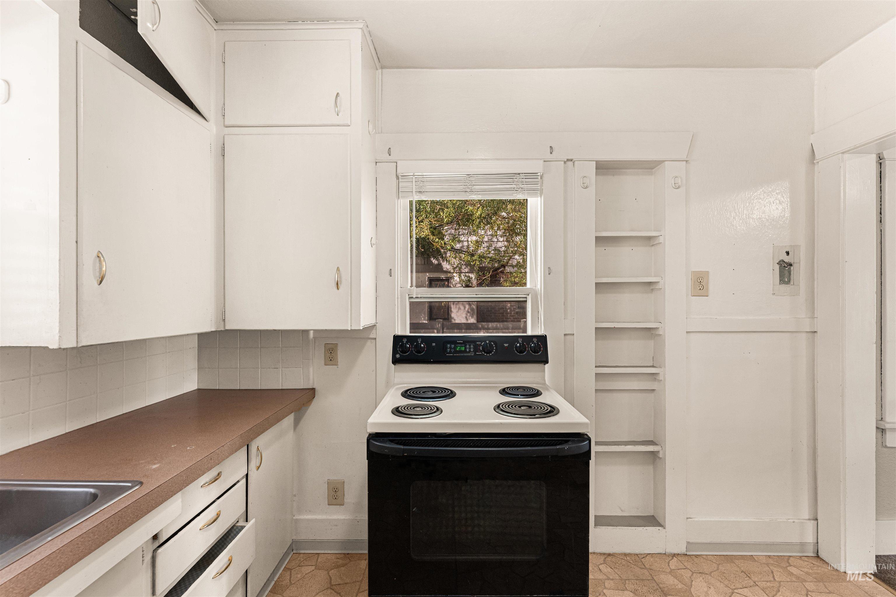 Kitchen with electric range oven, white cabinets, dark countertops, and backsplash