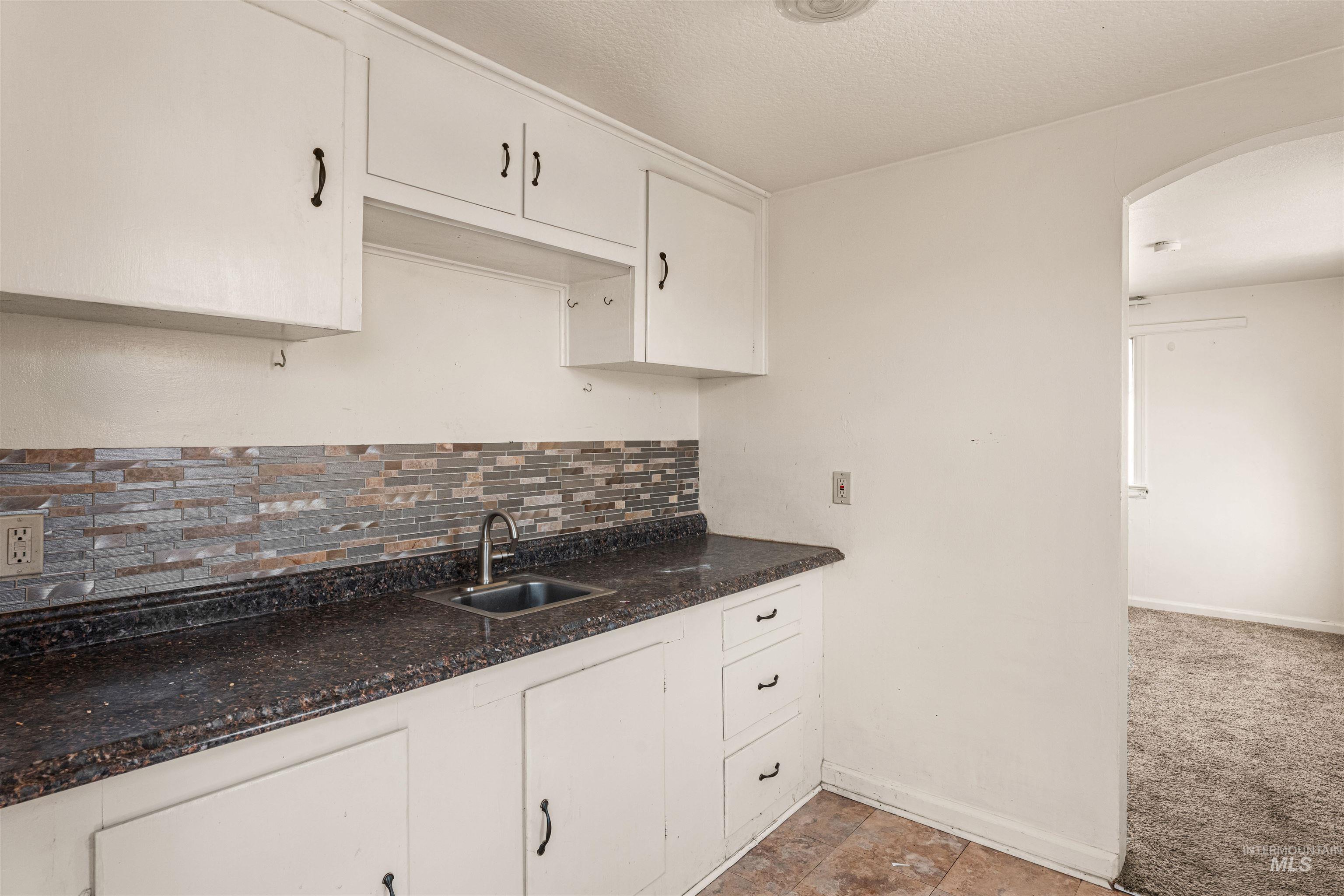 Kitchen with white cabinets, backsplash, arched walkways, a textured ceiling, and light carpet