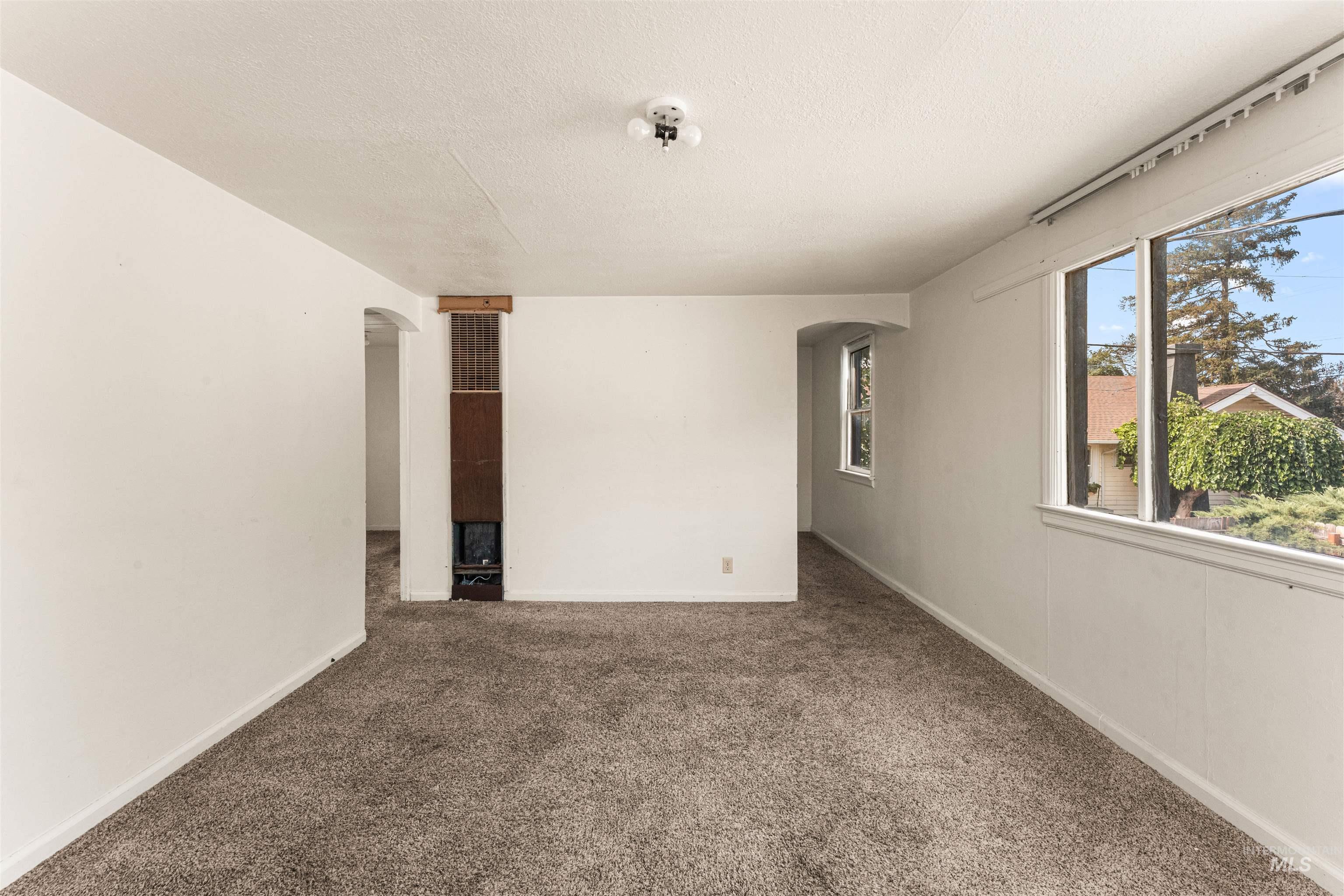 Unfurnished room with arched walkways, dark carpet, and a textured ceiling