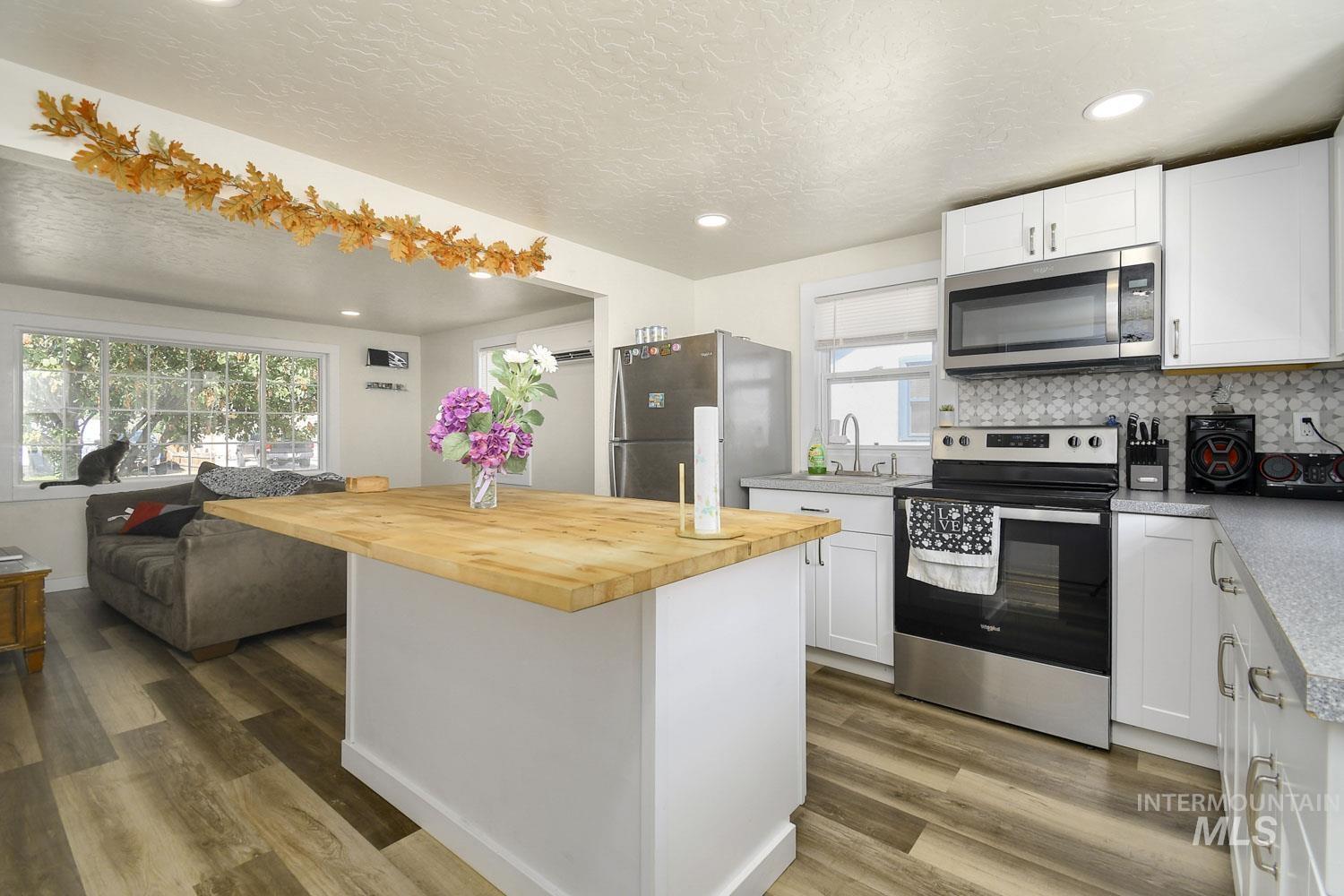 Kitchen with white cabinets, appliances with stainless steel finishes, decorative backsplash, light wood-style floors, and recessed lighting