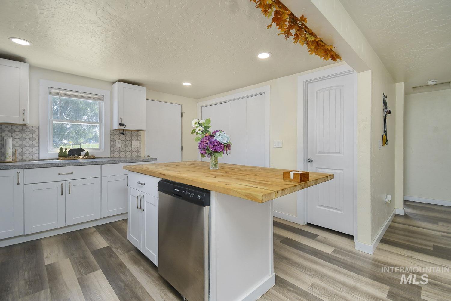 Kitchen with a textured ceiling, white cabinetry, butcher block countertops, dishwasher, and a kitchen island