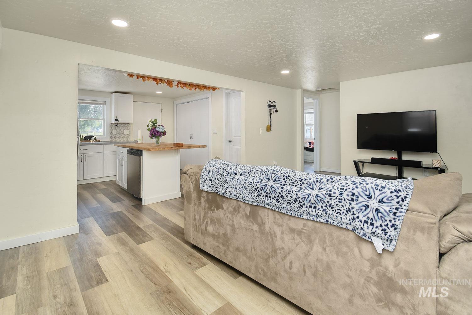 Living area with a textured ceiling, light wood-type flooring, and recessed lighting