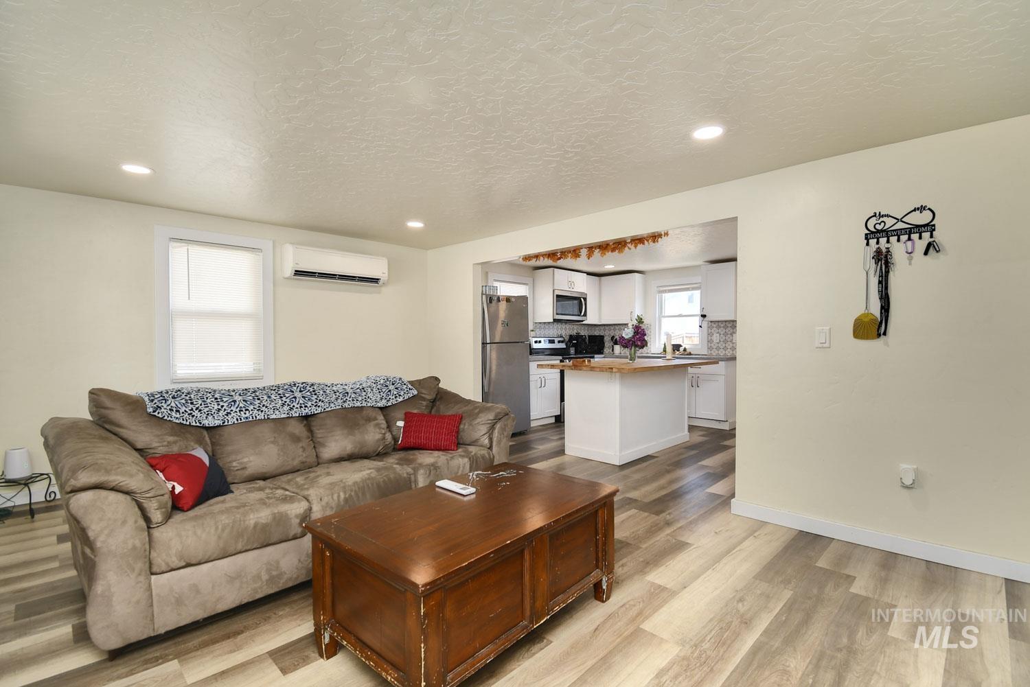 Living room with light wood finished floors, recessed lighting, an AC wall unit, and a textured ceiling