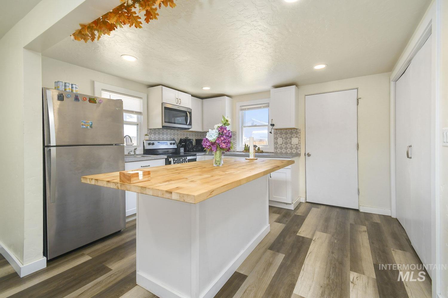 Kitchen with wooden counters, stainless steel appliances, white cabinets, a kitchen island, and backsplash