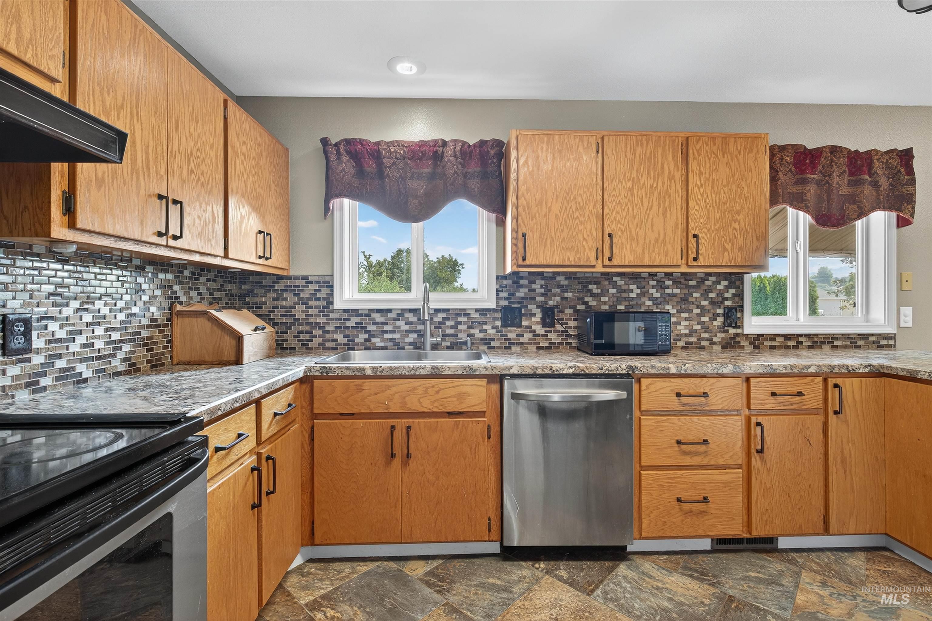Kitchen featuring stainless steel appliances, decorative backsplash, dark stone finish floors, brown cabinets, and under cabinet range hood