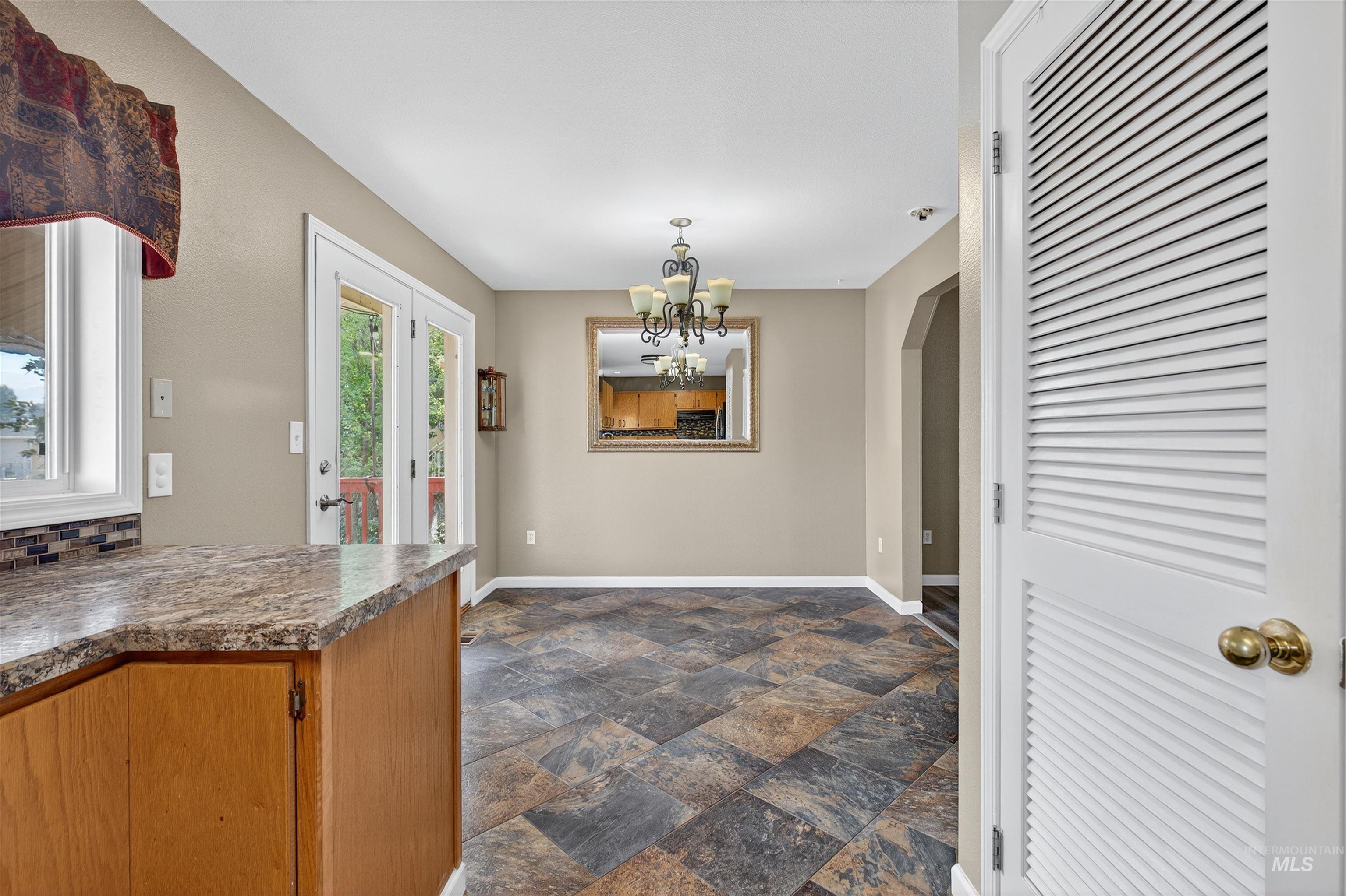 Kitchen with dark stone finish floors, brown cabinetry, a chandelier, dark countertops, and pendant lighting