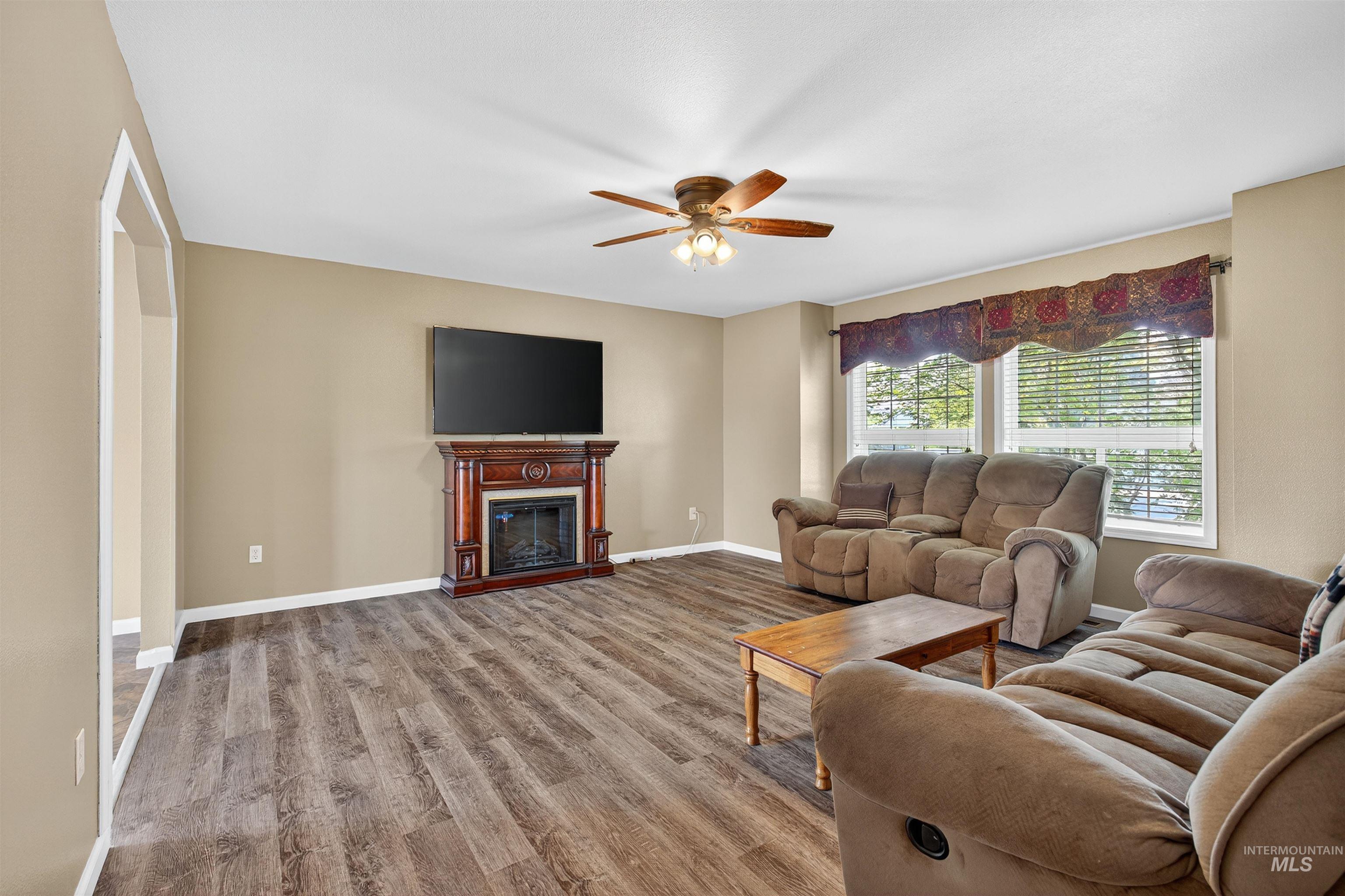 Living room featuring a glass covered fireplace, wood finished floors, and ceiling fan
