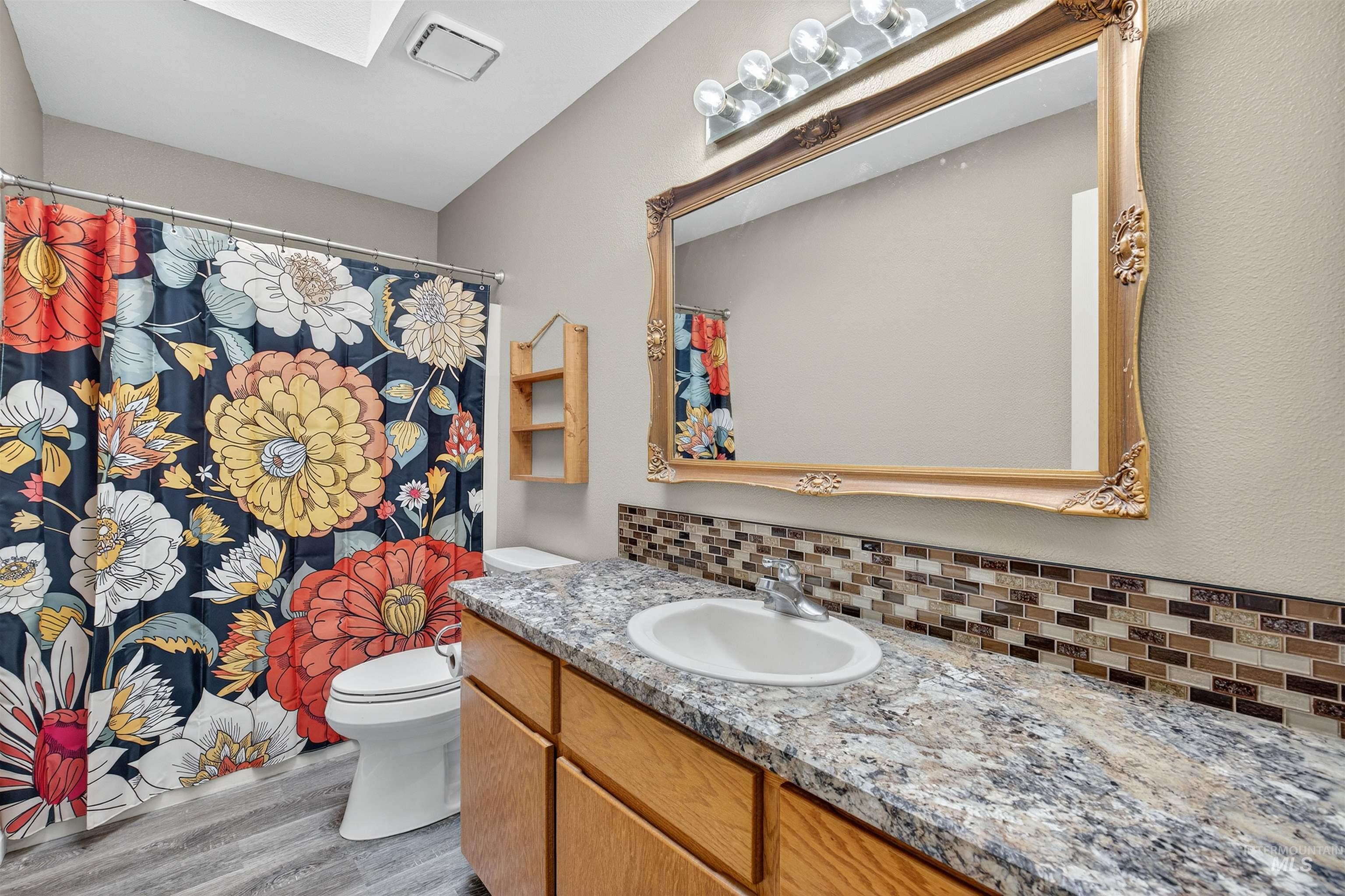 Bathroom featuring vanity, light wood-type flooring, tasteful backsplash, a shower with curtain, and a skylight