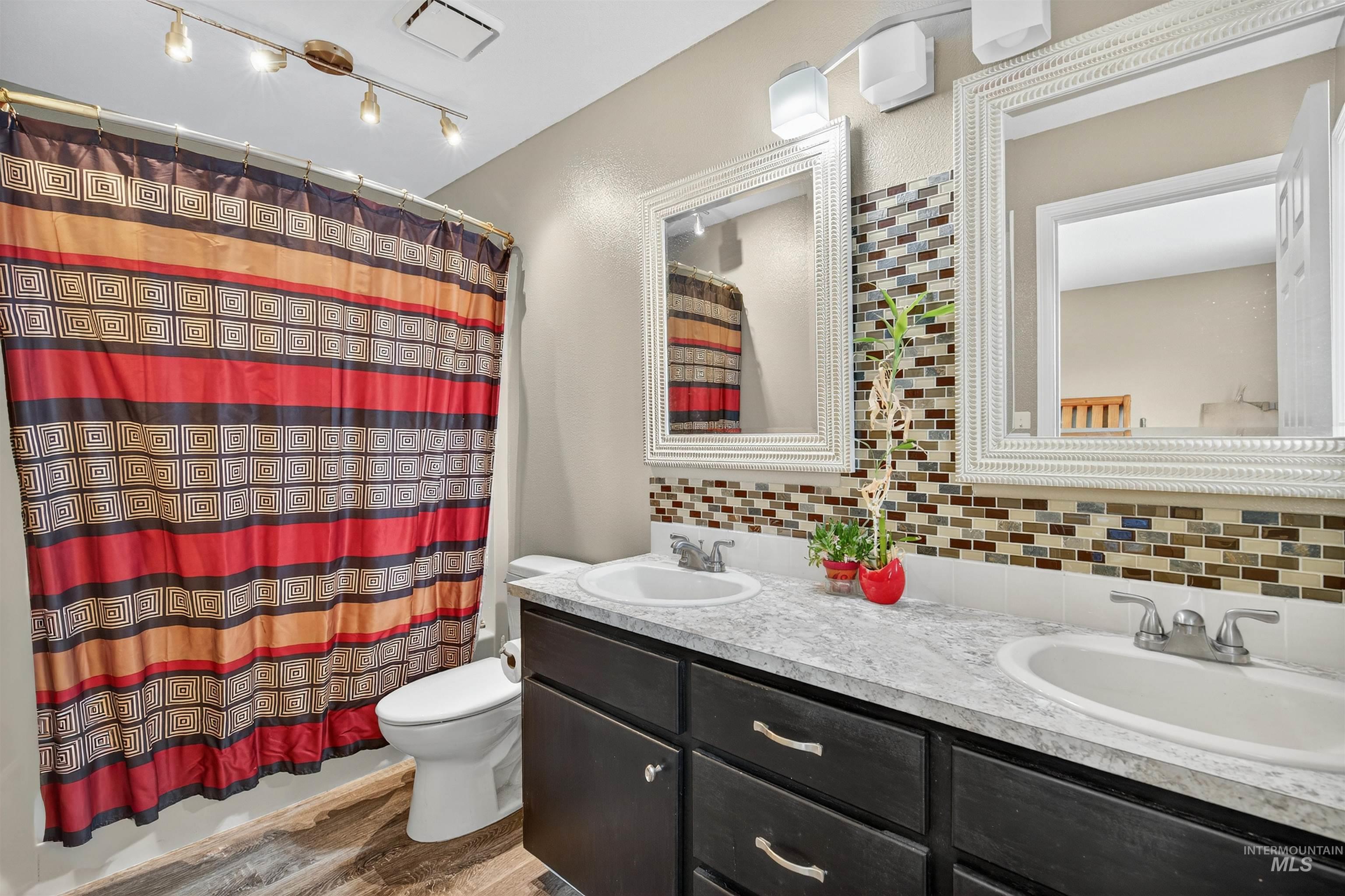 Bathroom with backsplash, double vanity, and dark wood-style floors