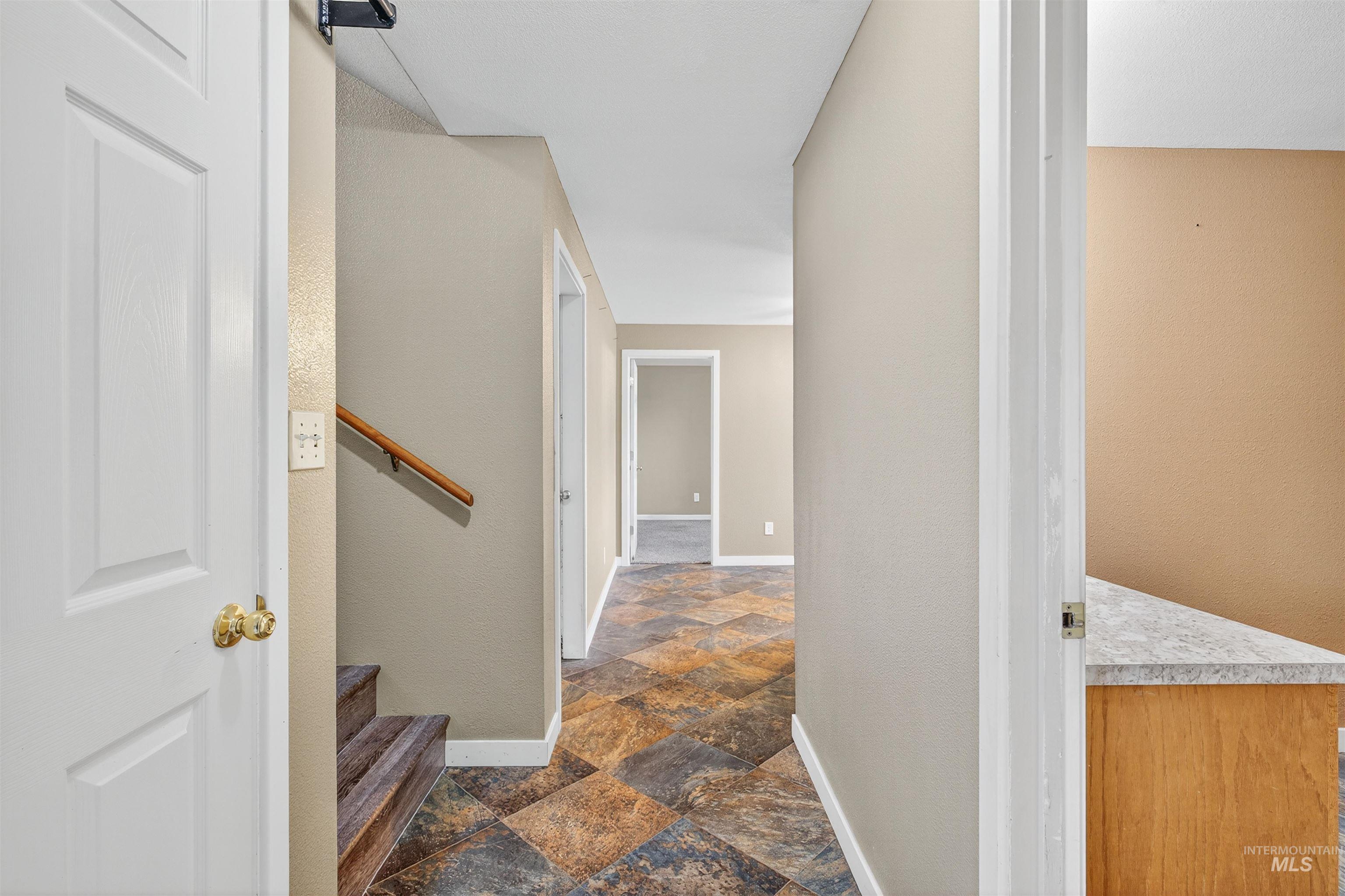 Hallway with dark stone finish floors, stairway, and a textured wall