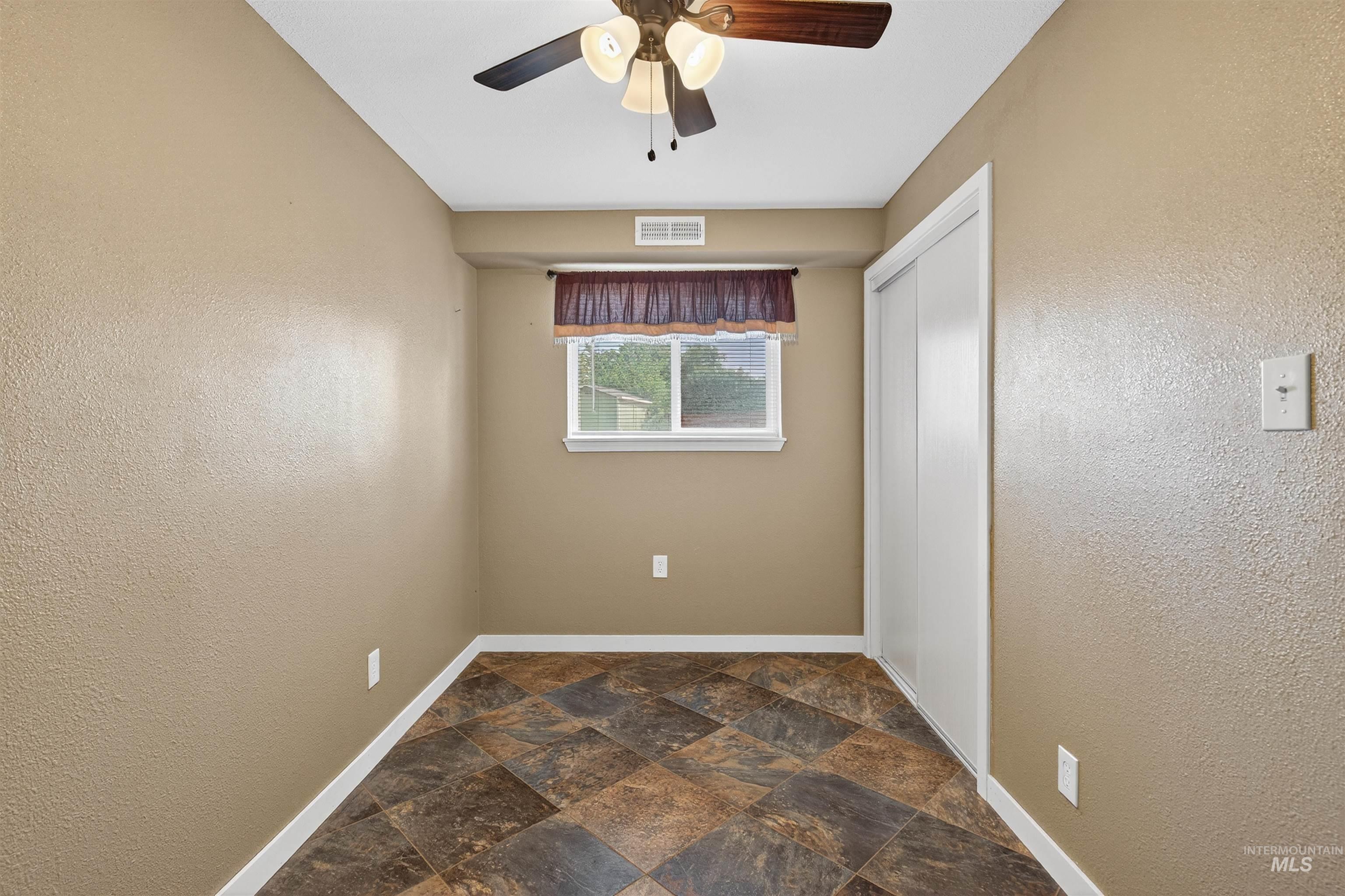 Unfurnished bedroom featuring a textured wall, dark stone finish flooring, a ceiling fan, and a closet