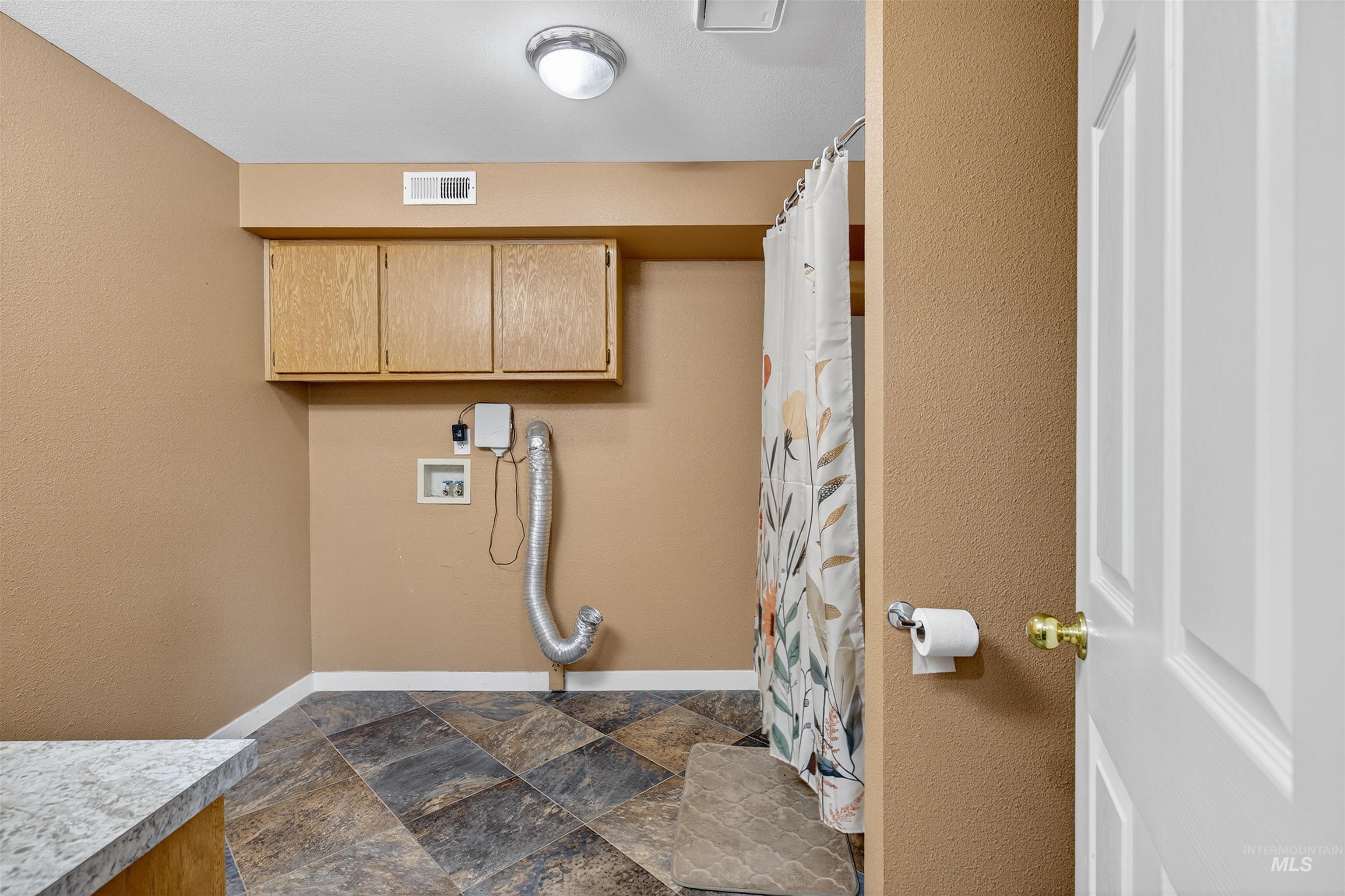 Laundry room featuring cabinet space, dark stone finish flooring, washer hookup, and a textured wall