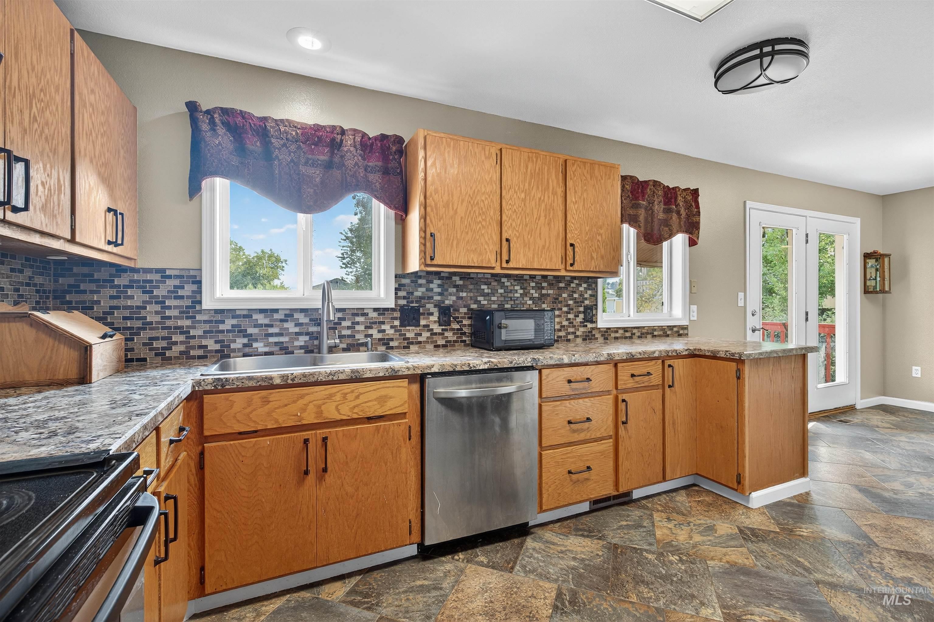 Kitchen featuring electric stove, dishwasher, decorative backsplash, brown cabinets, and dark stone finish floors